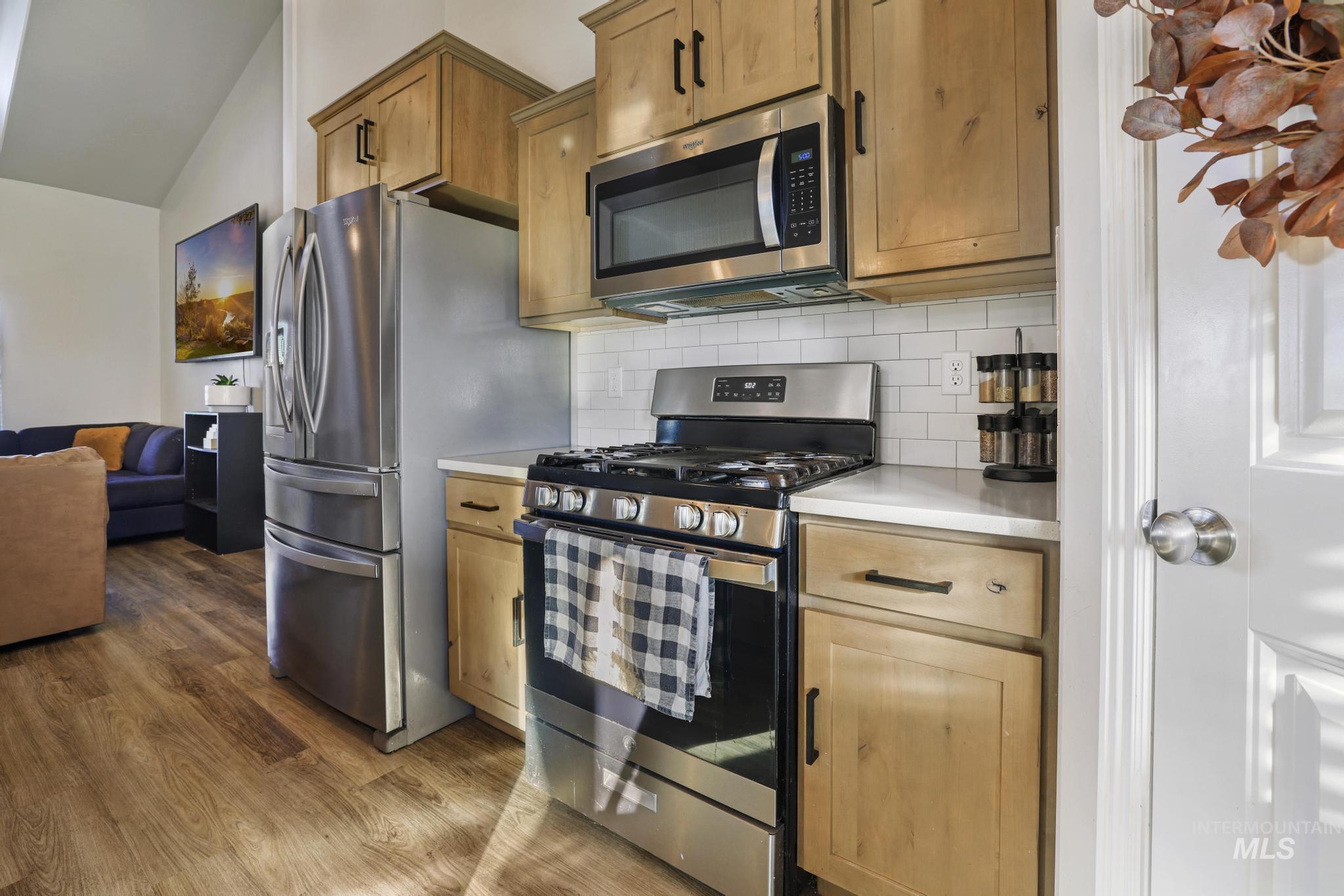 Kitchen with stainless steel appliances, light countertops, tasteful backsplash, vaulted ceiling, and dark wood-style floors