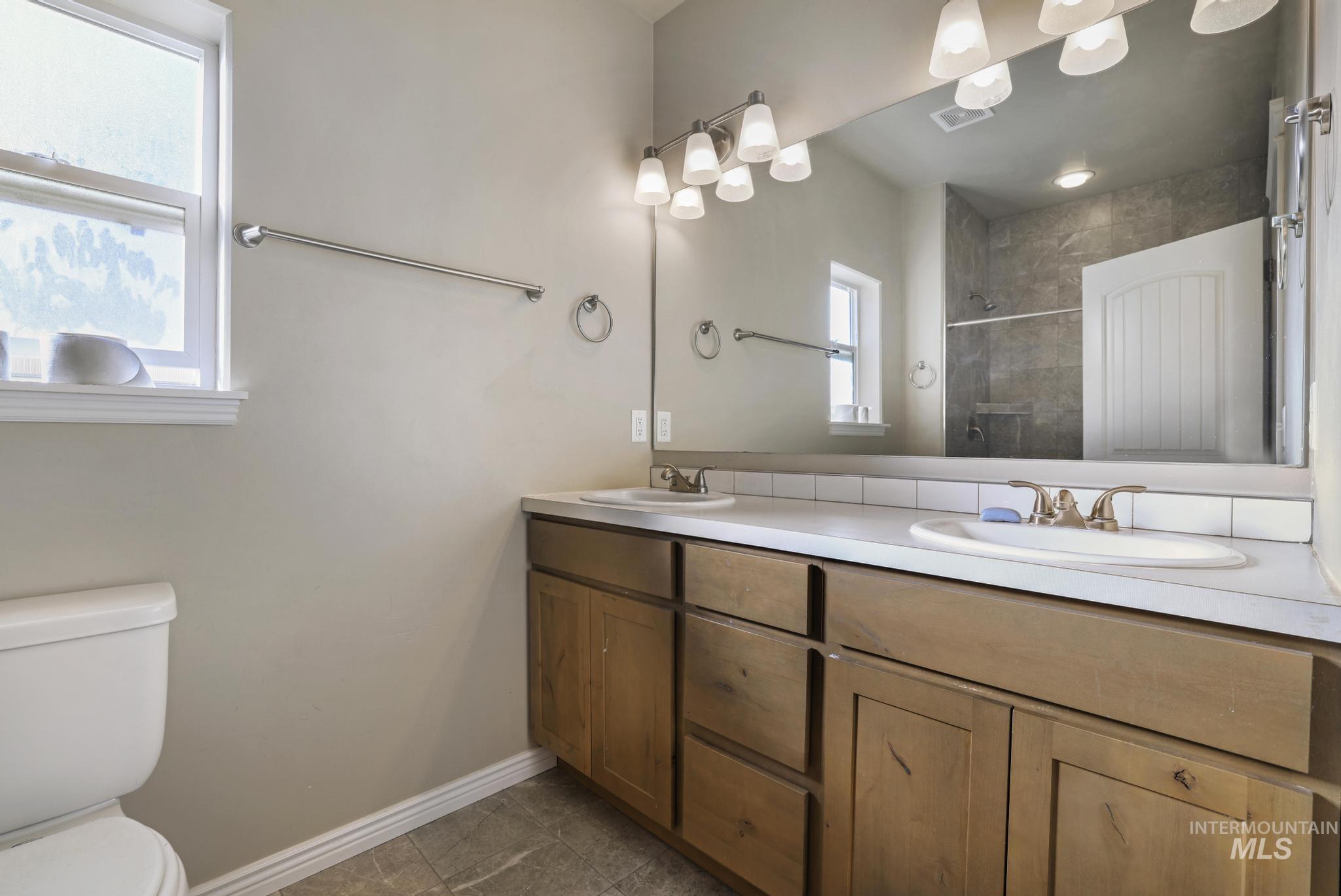 Full bath featuring double vanity, a shower stall, and dark tile patterned floors
