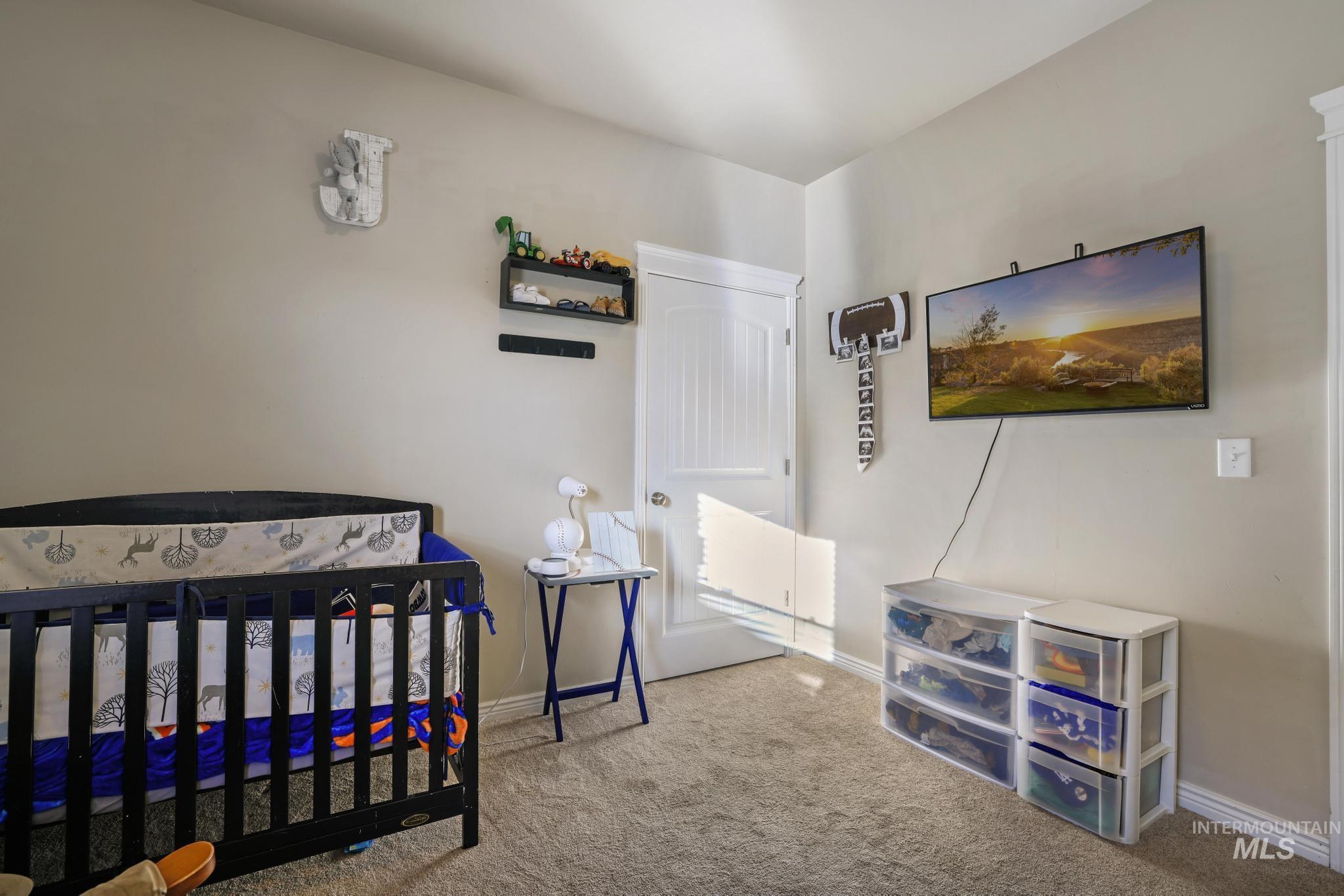 Carpeted bedroom featuring a nursery area and baseboards