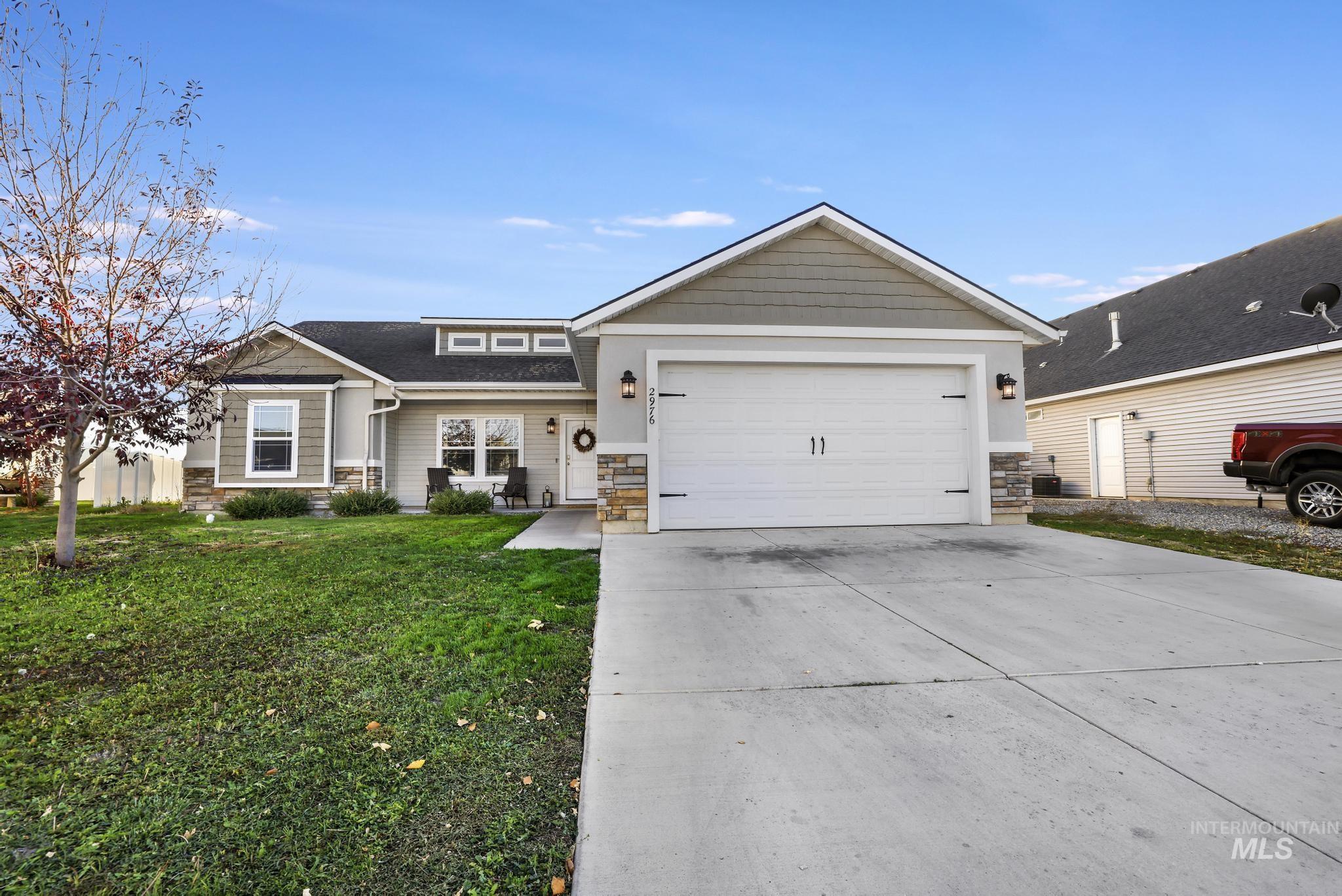View of front of home with stone siding, driveway, a front lawn, a garage, and a shingled roof