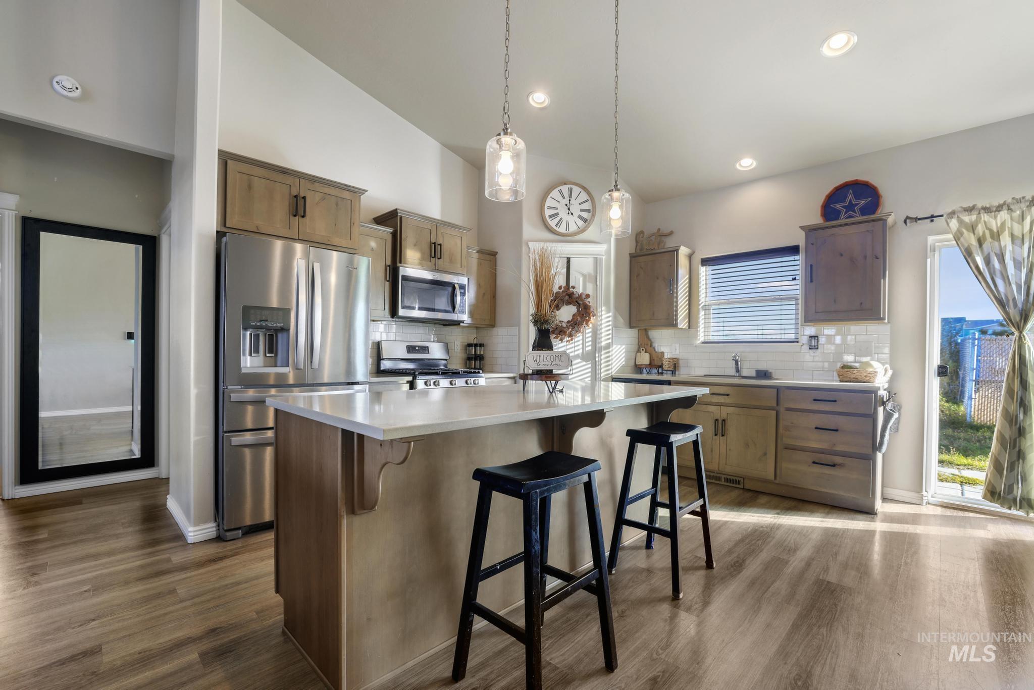 Kitchen with stainless steel appliances, light countertops, decorative backsplash, a breakfast bar area, and decorative light fixtures