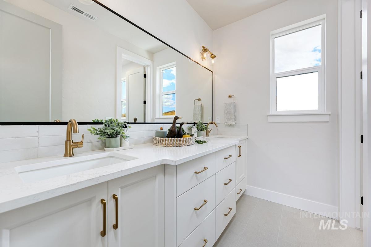 Bathroom featuring double vanity, tasteful backsplash, and light tile patterned floors