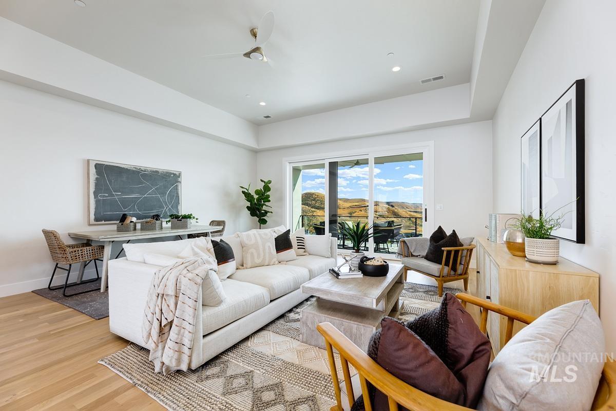 Living room featuring light wood finished floors, recessed lighting, ceiling fan, and a tray ceiling