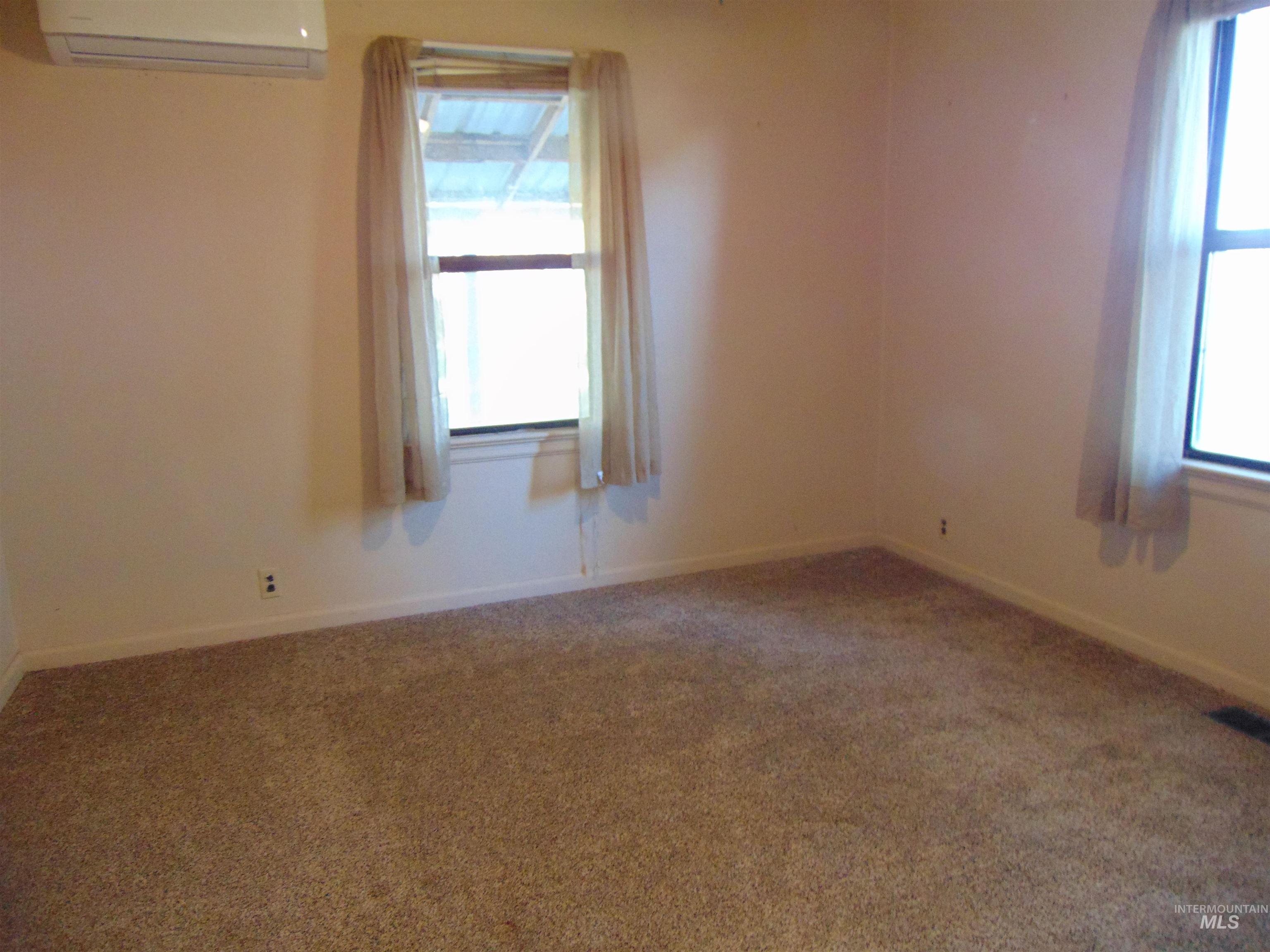 Carpeted empty room with a wall mounted AC and baseboards