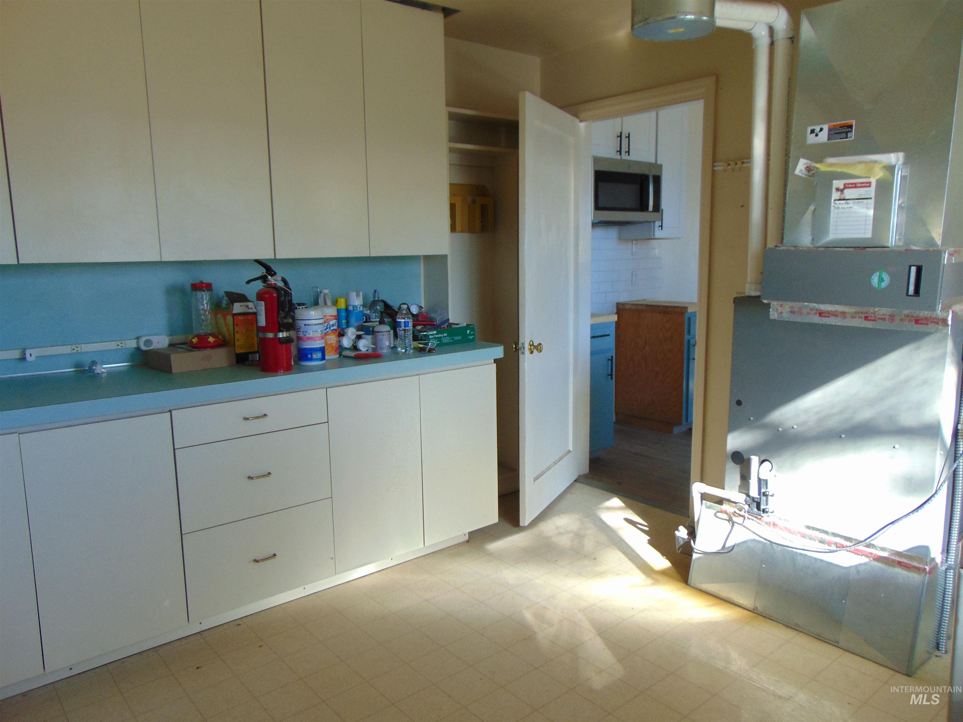 Kitchen featuring light floors, heating unit, white cabinetry, stainless steel microwave, and light countertops