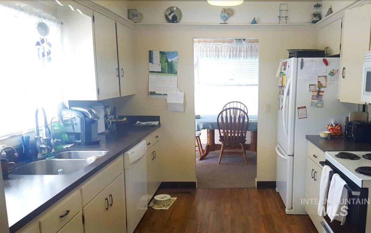 Kitchen featuring dark countertops, dark wood-style flooring, white appliances, and white cabinetry