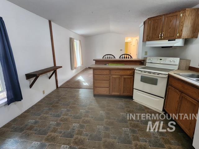 Kitchen featuring electric stove, stone finish floors, a peninsula, vaulted ceiling, and brown cabinets