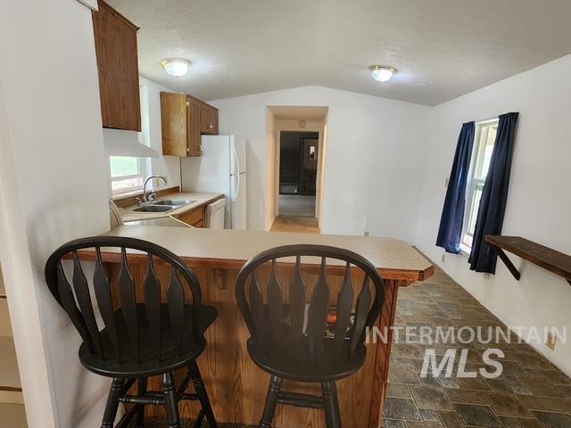 Kitchen featuring light countertops, stone finish flooring, brown cabinets, a peninsula, and a kitchen bar