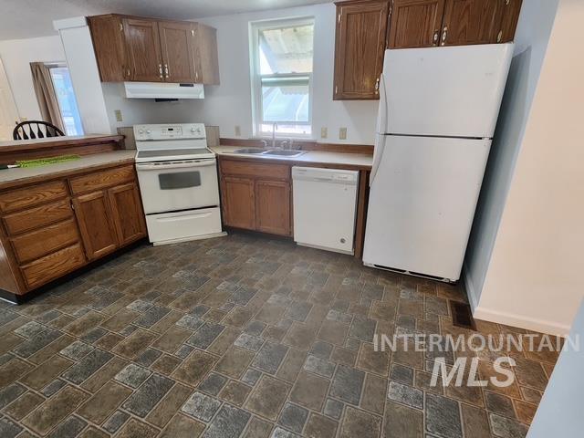 Kitchen featuring white appliances, brown cabinetry, under cabinet range hood, and light countertops