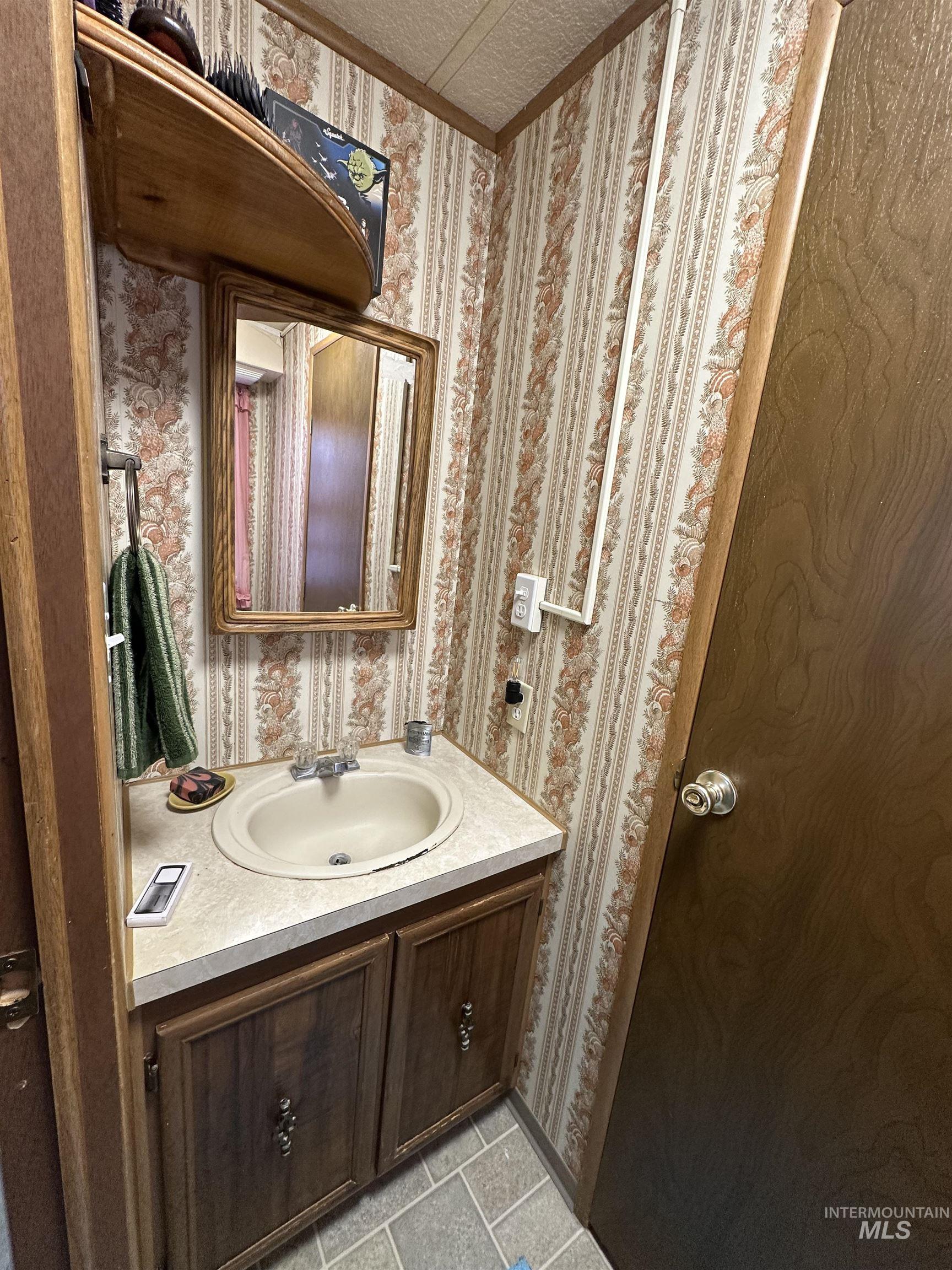 Bathroom featuring wallpapered walls, vanity, and light tile patterned flooring