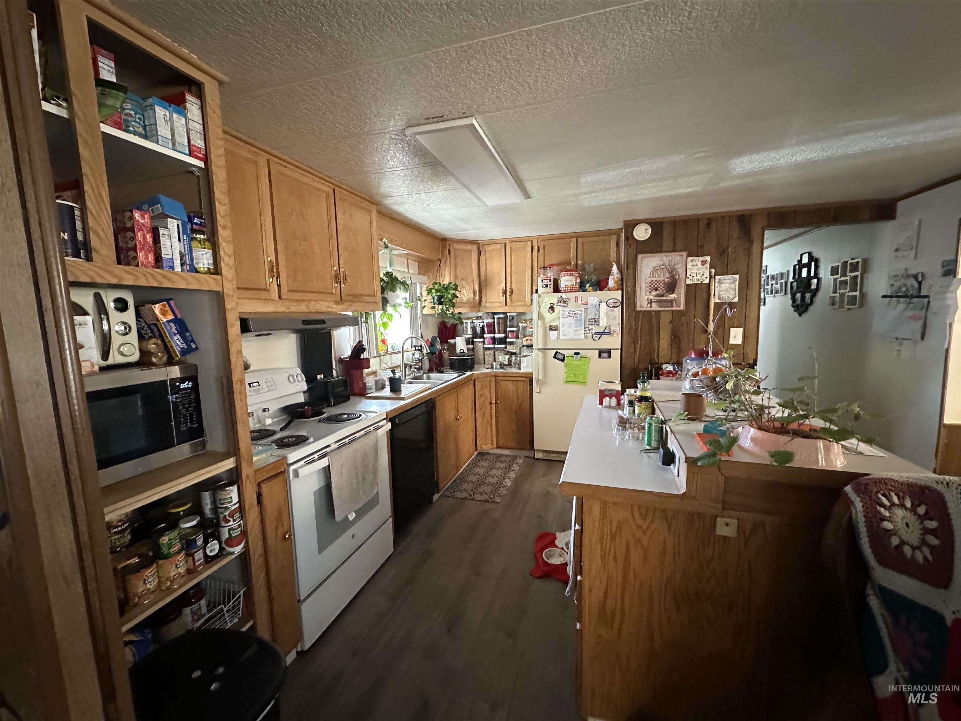 Kitchen with white appliances, dark wood-style floors, light countertops, a textured ceiling, and brown cabinetry