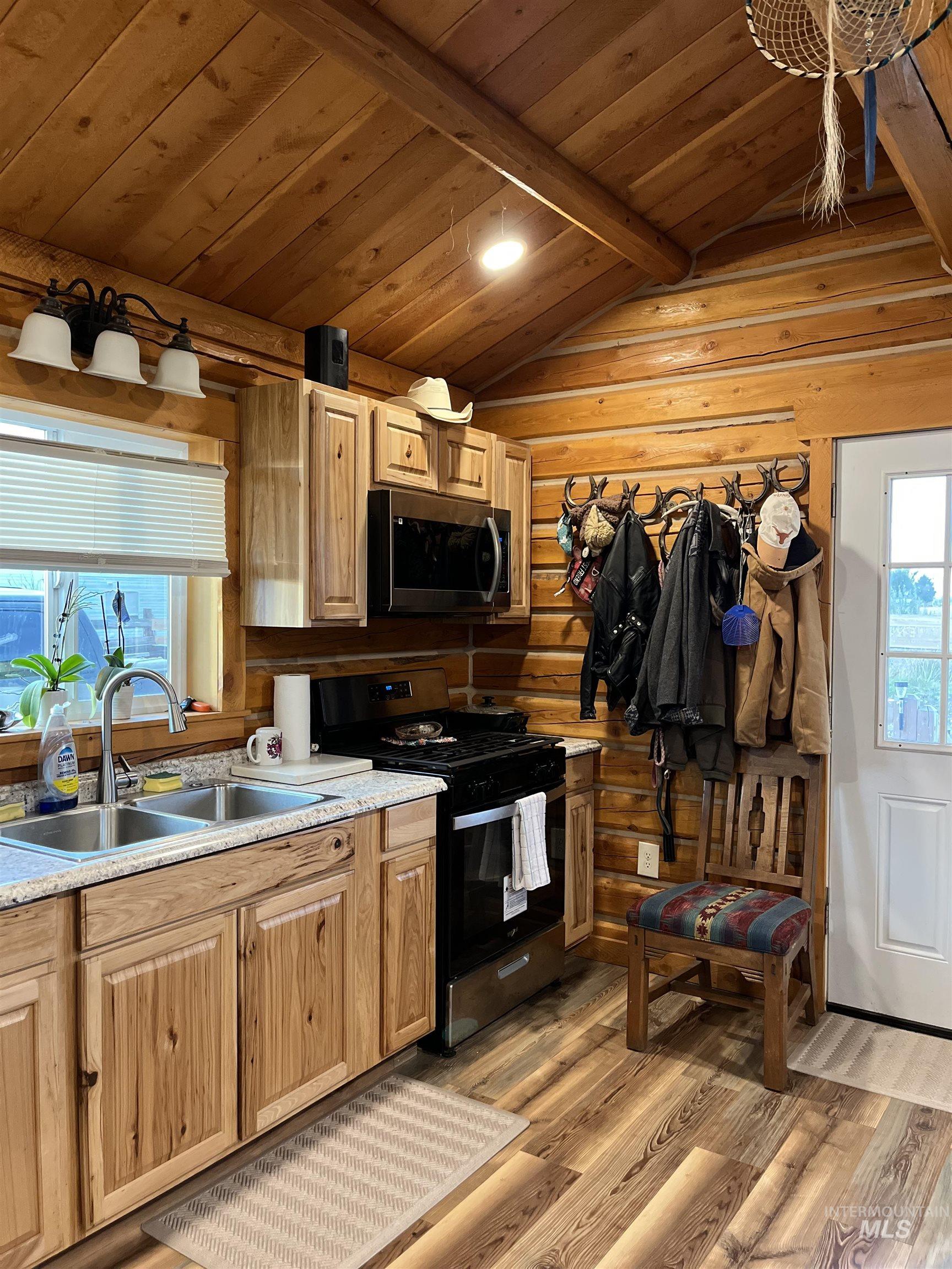 Kitchen featuring black gas stove, wooden ceiling, light wood-style floors, light countertops, and stainless steel microwave