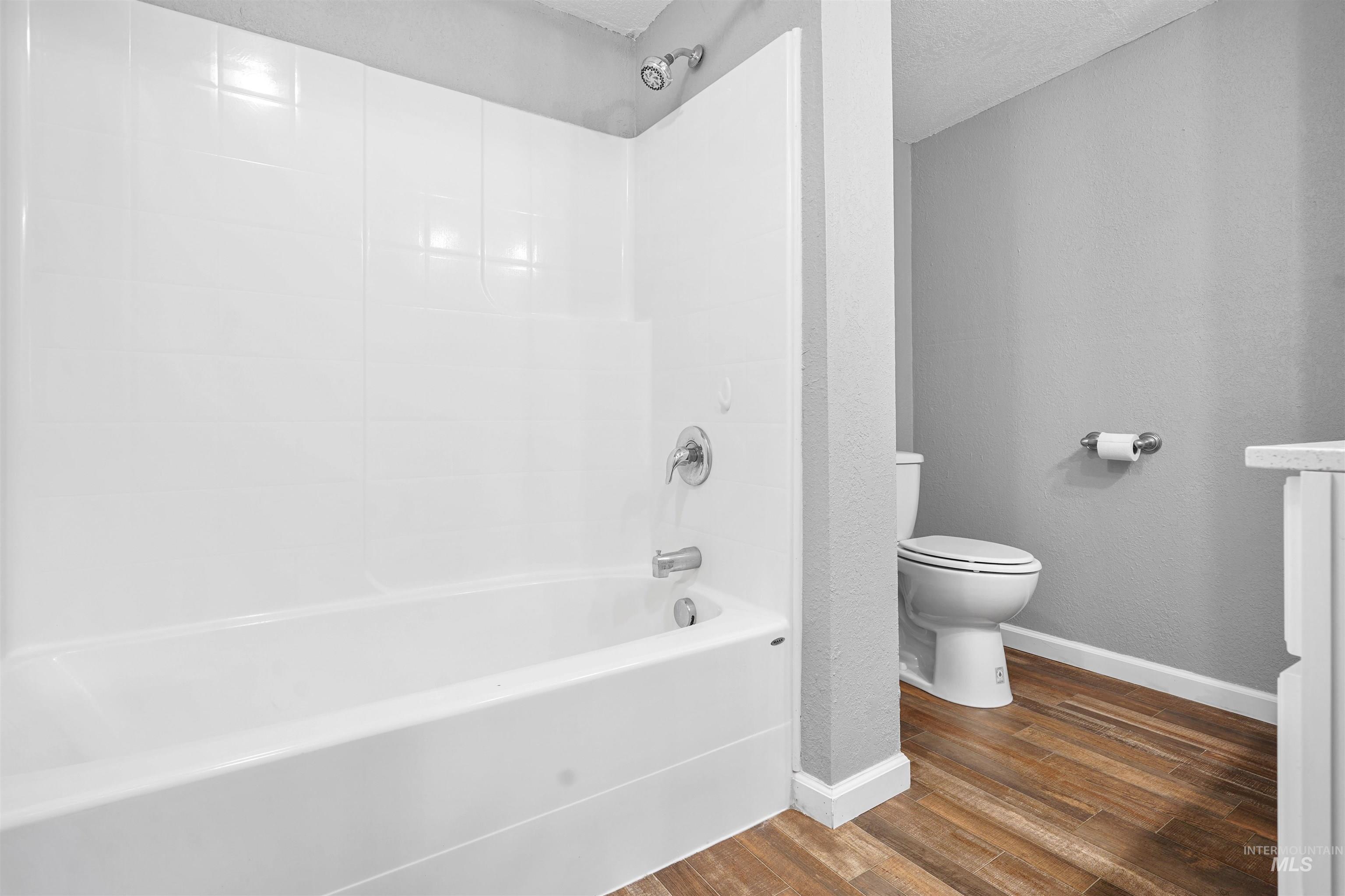 Bathroom with dark wood-style flooring, vanity, shower / washtub combination, a textured ceiling, and a textured wall