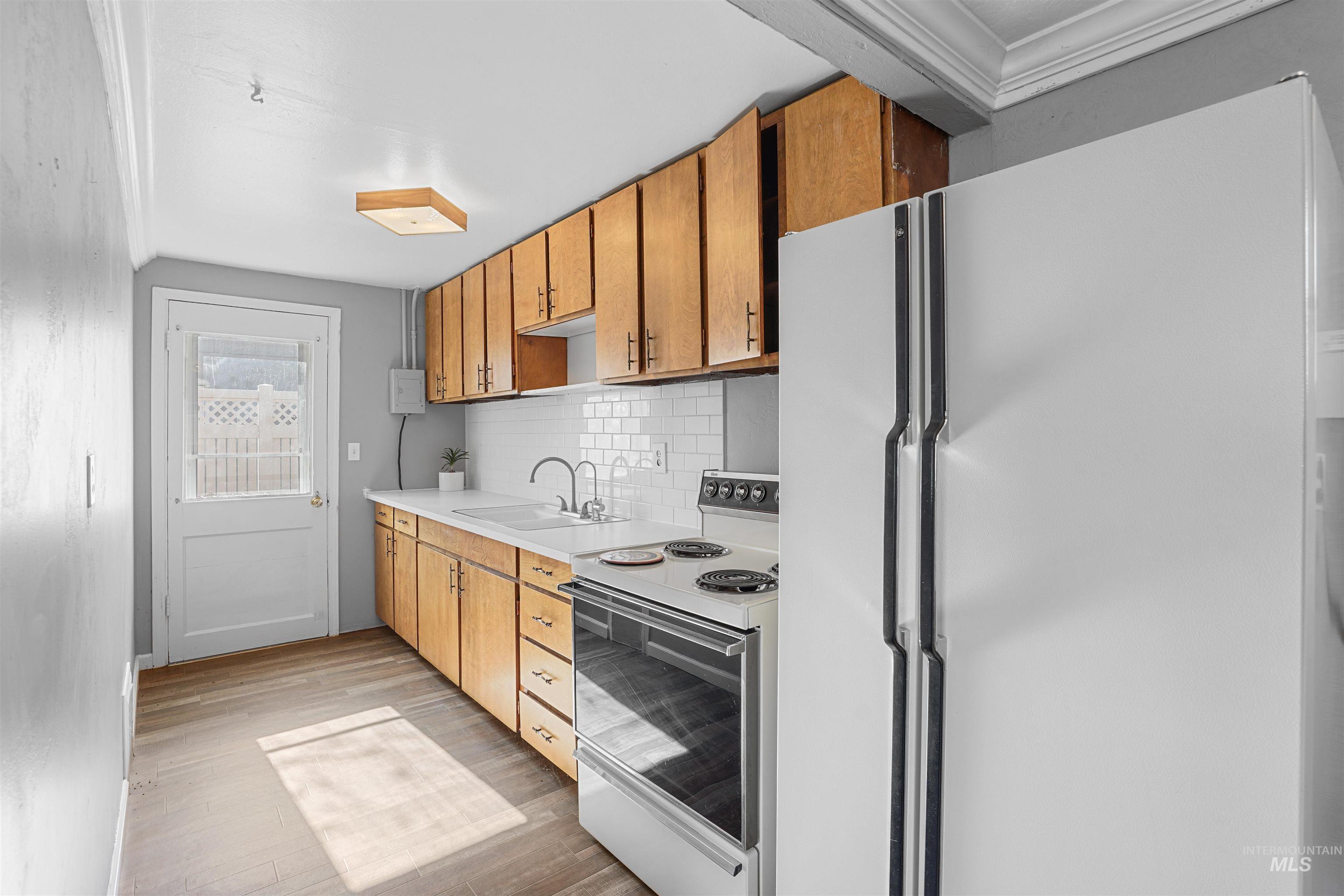 Kitchen with white appliances, light countertops, backsplash, light wood finished floors, and brown cabinetry
