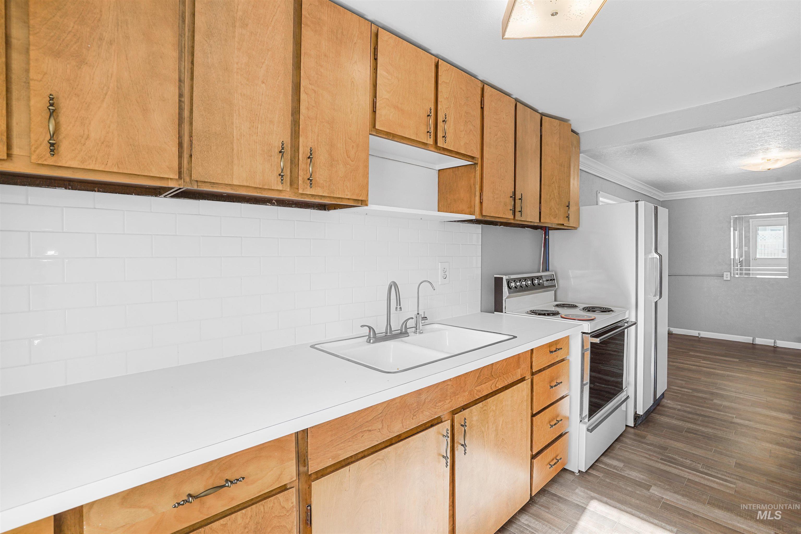 Kitchen with electric range, light countertops, crown molding, decorative backsplash, and light wood-type flooring