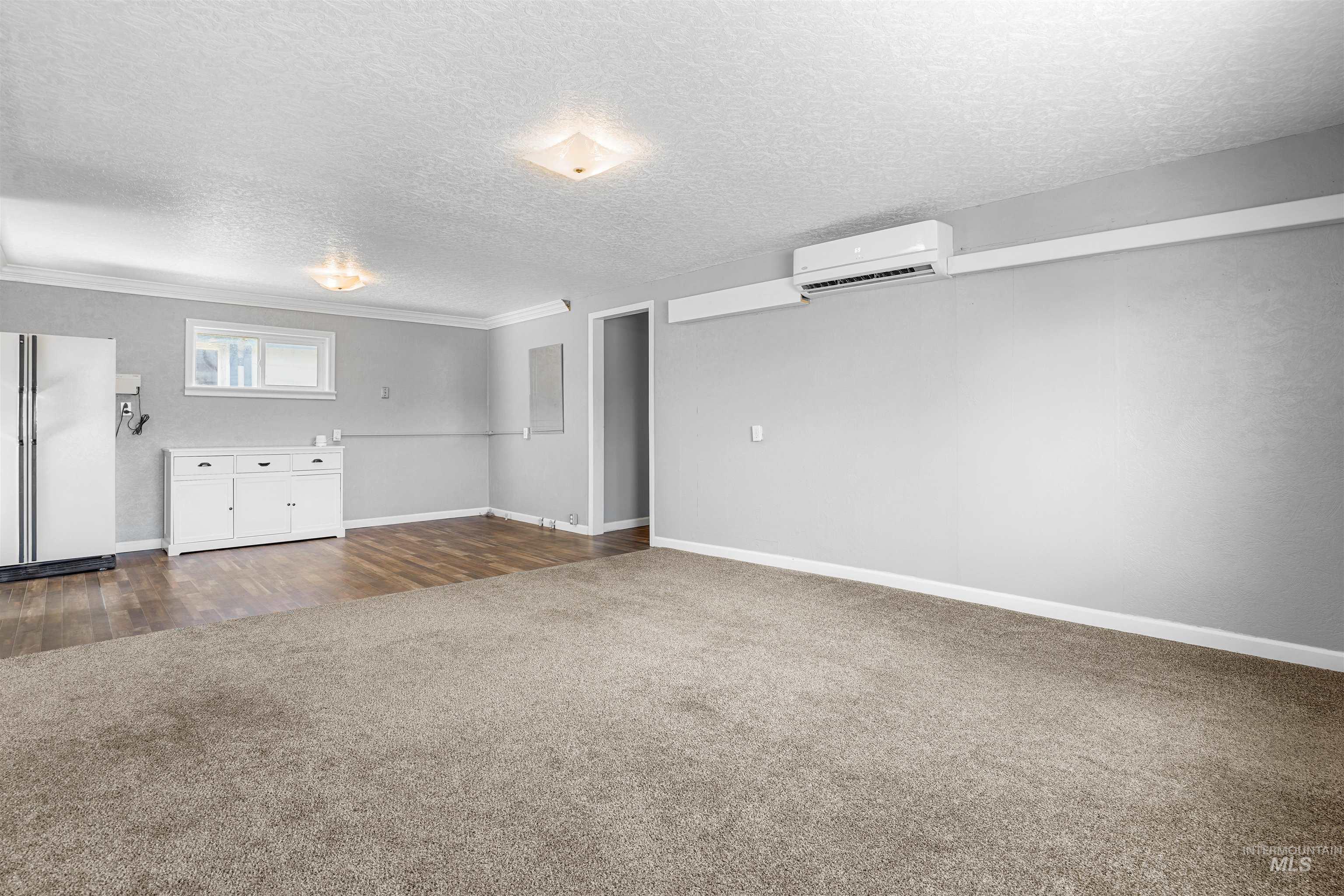 Unfurnished living room featuring dark colored carpet, a textured ceiling, and a wall mounted air conditioner