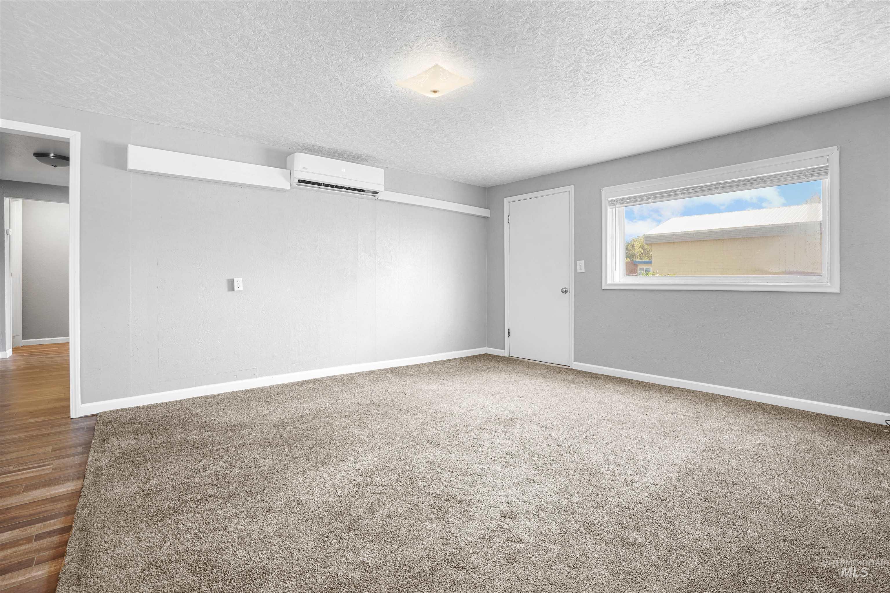 Spare room featuring a textured ceiling, light carpet, and an AC wall unit