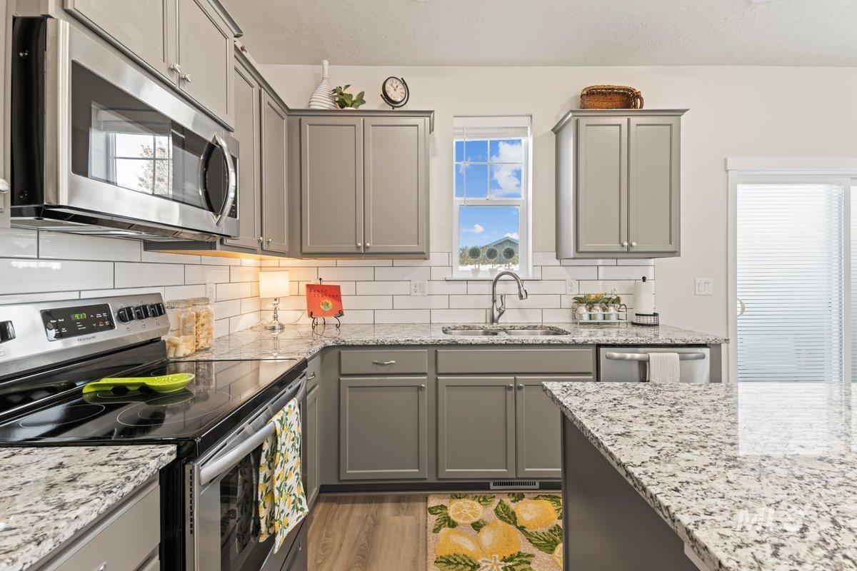 Kitchen with appliances with stainless steel finishes, gray cabinetry, light wood-style flooring, tasteful backsplash, and a textured ceiling