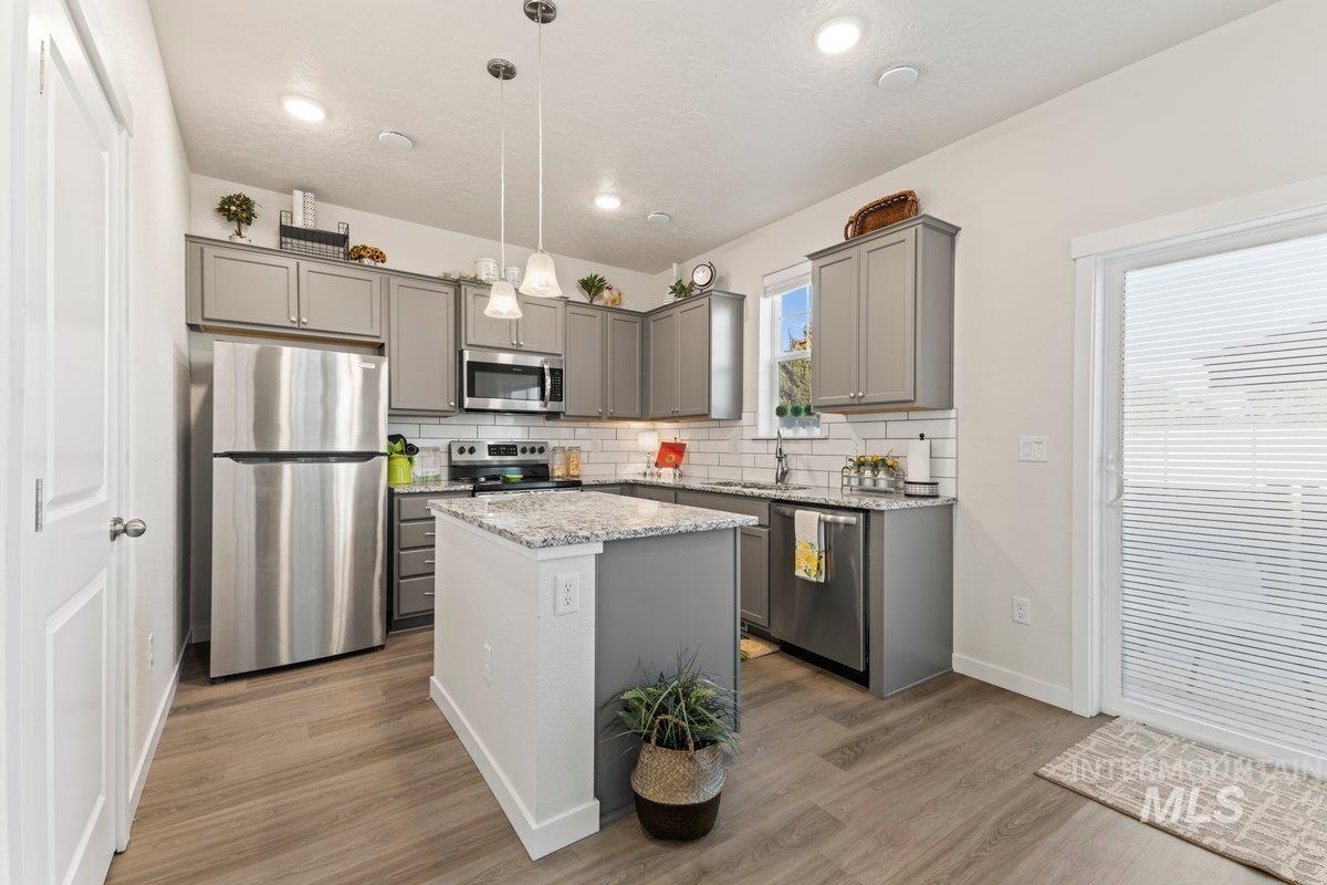 Kitchen featuring gray cabinetry, pendant lighting, appliances with stainless steel finishes, tasteful backsplash, and light stone countertops