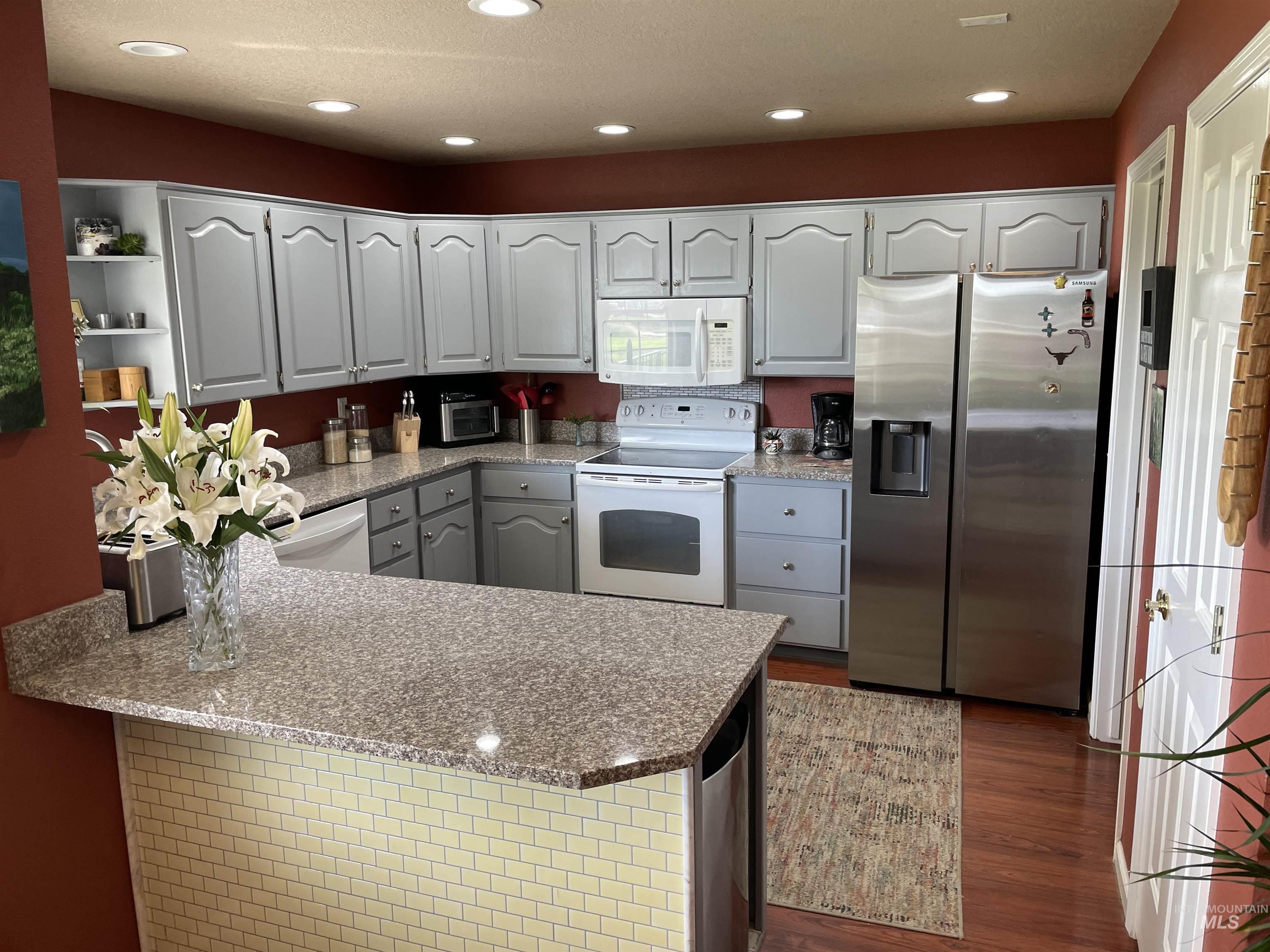 Kitchen with white appliances, light stone counters, recessed lighting, a peninsula, and dark wood-style flooring