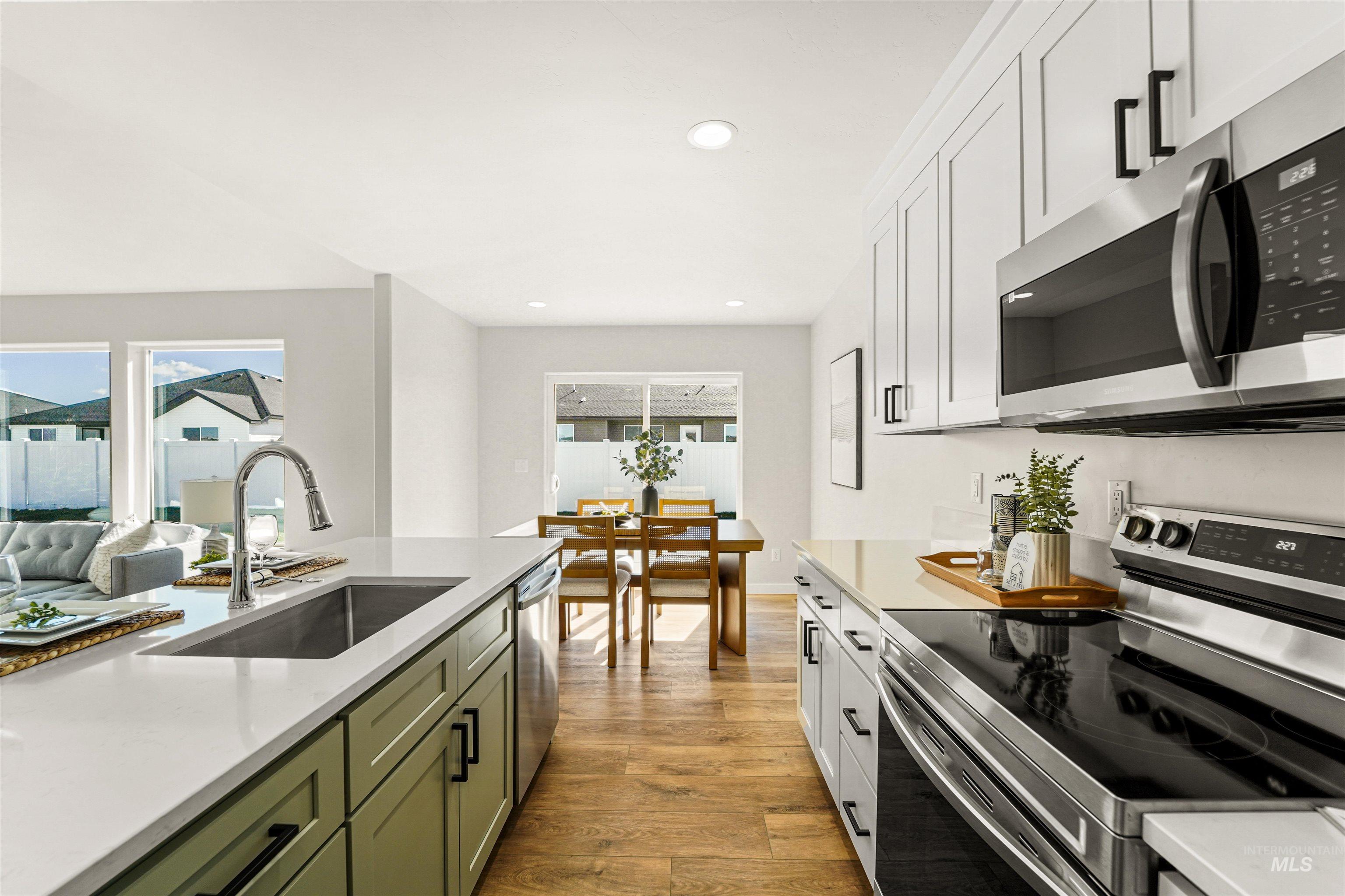 Kitchen featuring appliances with stainless steel finishes, green cabinetry, white cabinetry, light stone countertops, and recessed lighting