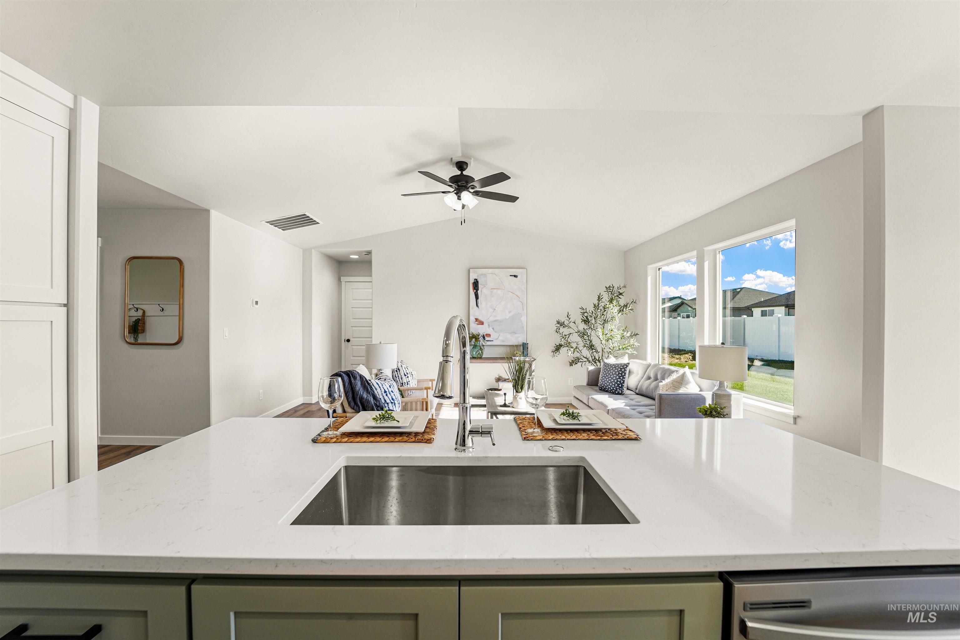 Kitchen featuring green cabinets, open floor plan, light stone countertops, a center island with sink, and stainless steel dishwasher