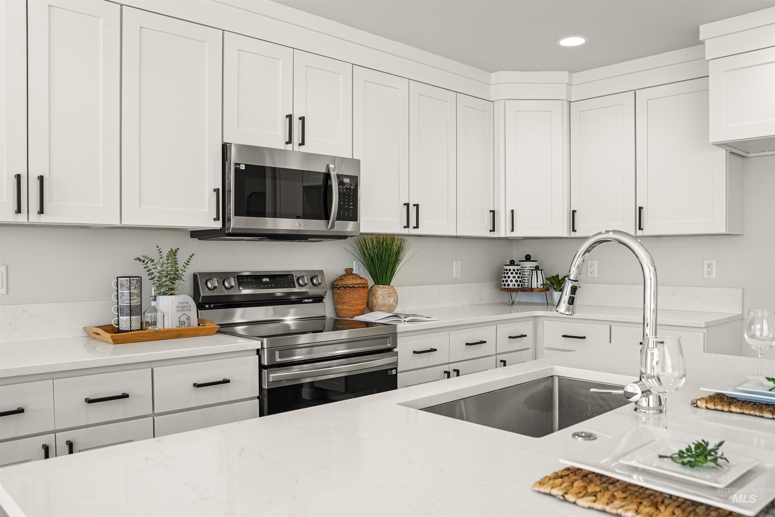 Kitchen featuring stainless steel appliances, white cabinets, light stone counters, and recessed lighting