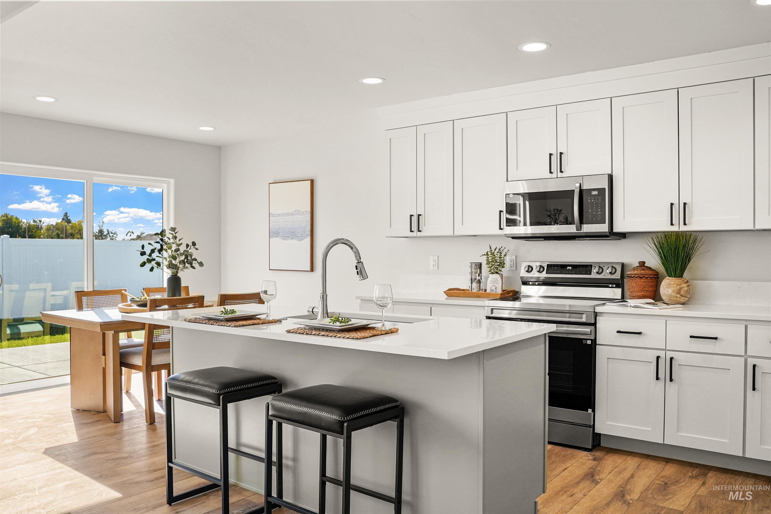 Kitchen featuring appliances with stainless steel finishes, recessed lighting, a kitchen island with sink, white cabinetry, and light wood finished floors