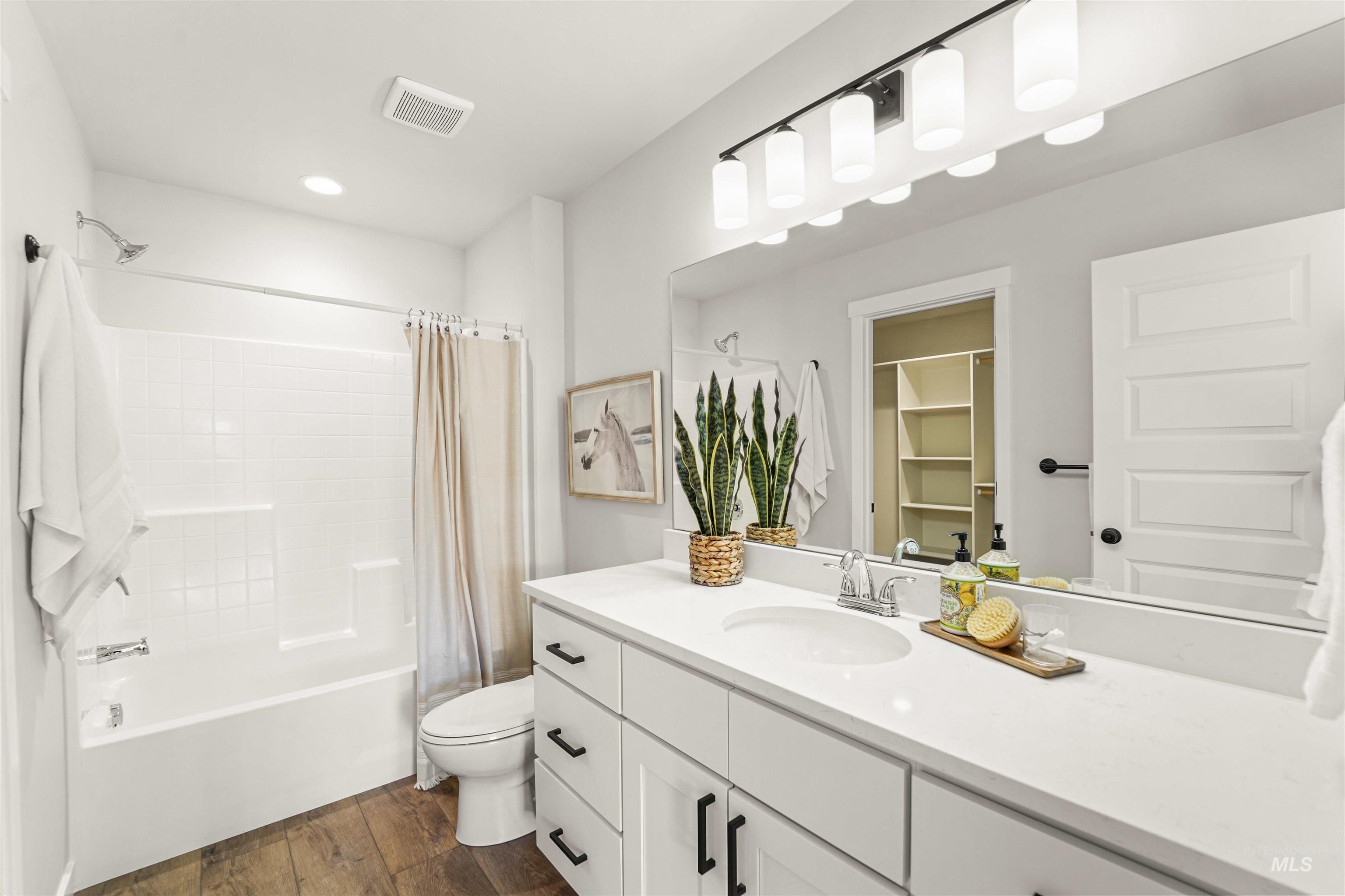 Bathroom with shower / bathtub combination with curtain, vanity, dark wood-style flooring, and a spacious closet