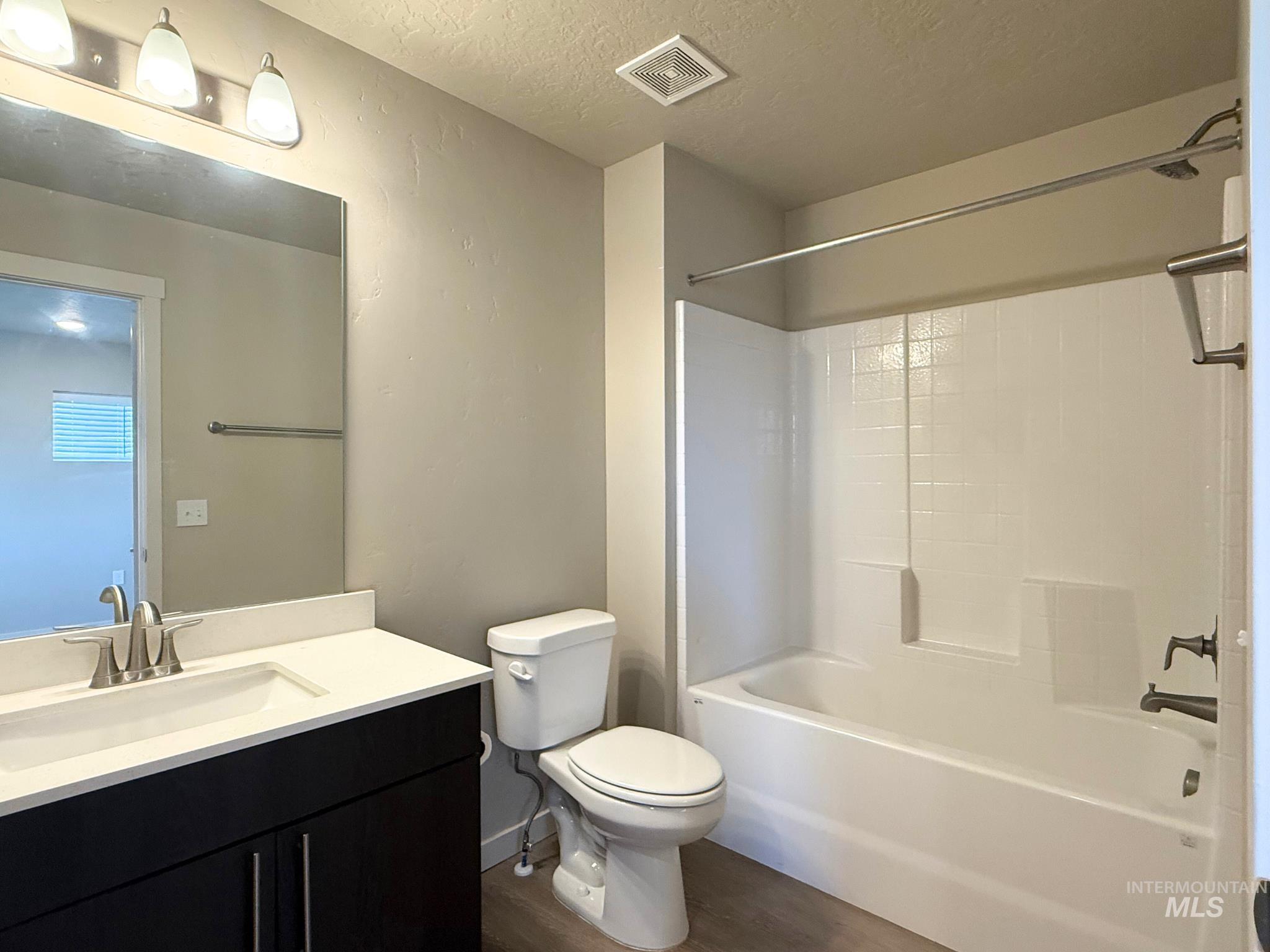 Full bathroom with vanity, dark wood finished floors, a textured ceiling, and shower / washtub combination