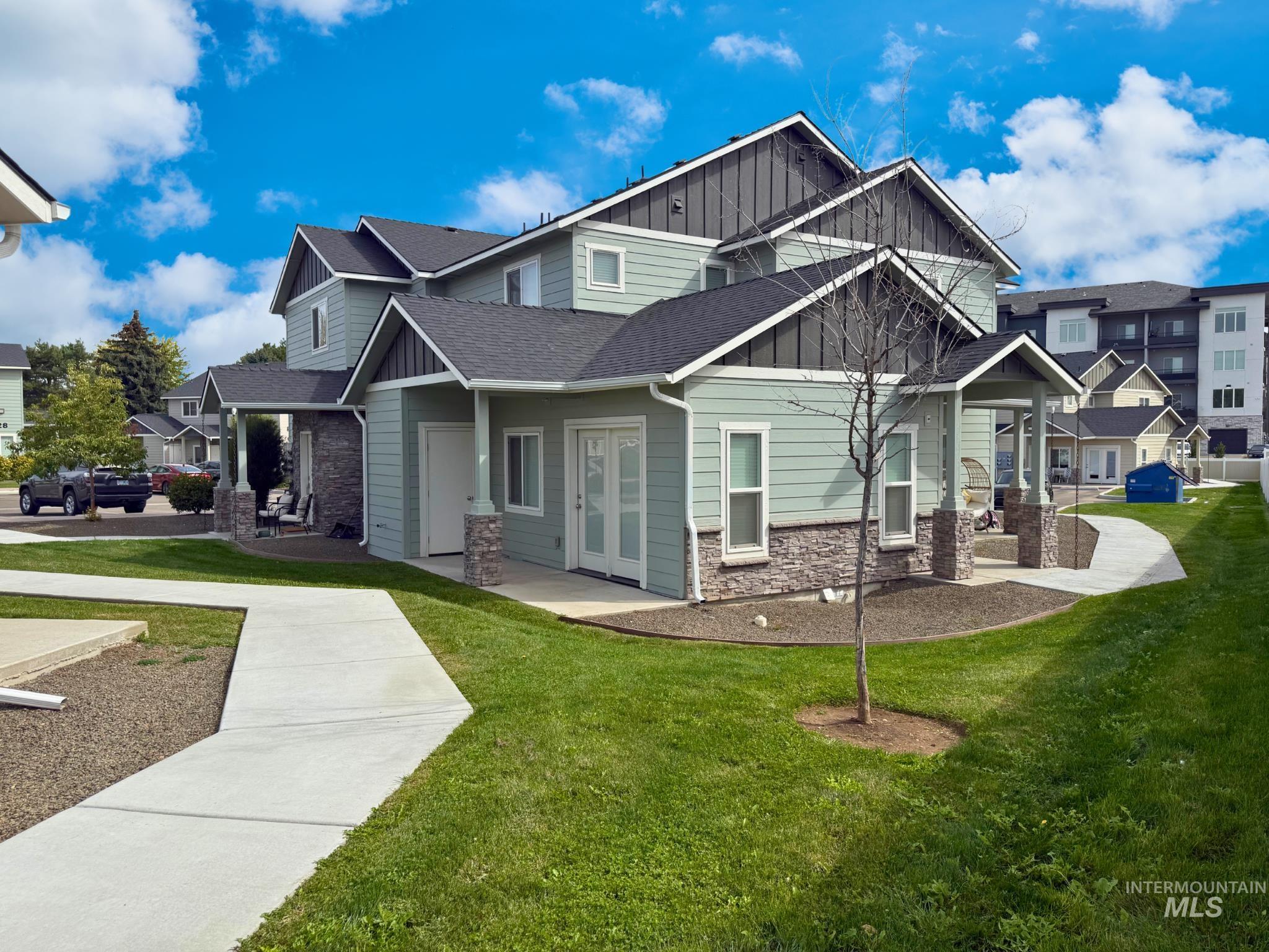View of front of house with board and batten siding, stone siding, a front lawn, a shingled roof, and covered porch