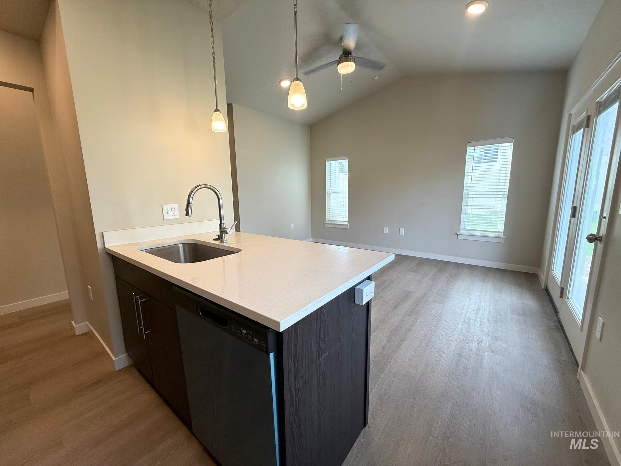 Kitchen with dishwasher, light wood-style flooring, pendant lighting, vaulted ceiling, and open floor plan