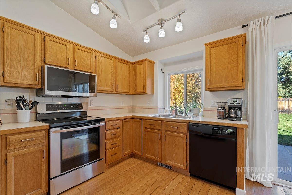 Kitchen with stainless steel appliances, light countertops, light wood-type flooring, and lofted ceiling
