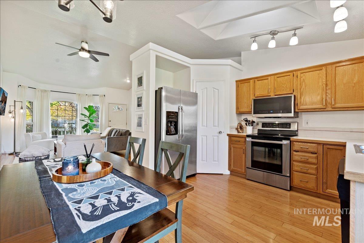 Kitchen featuring stainless steel appliances, light countertops, lofted ceiling, light wood-style floors, and brown cabinets