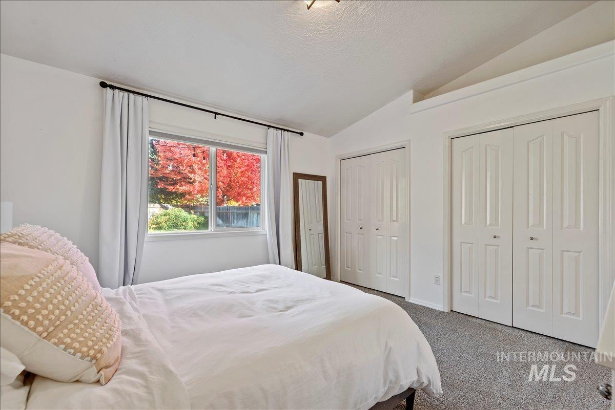 Bedroom with lofted ceiling, two closets, carpet flooring, and a textured ceiling
