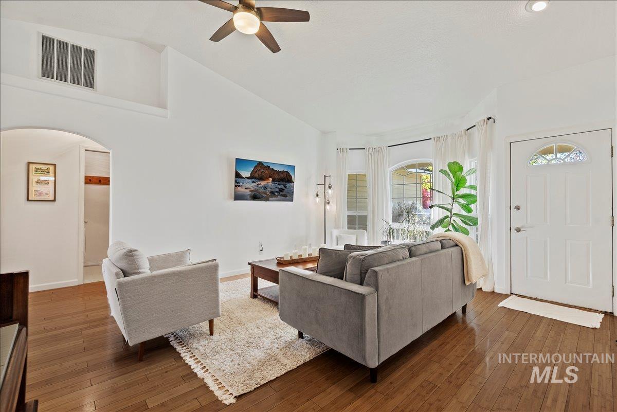 Living room with hardwood / wood-style flooring, arched walkways, ceiling fan, and high vaulted ceiling