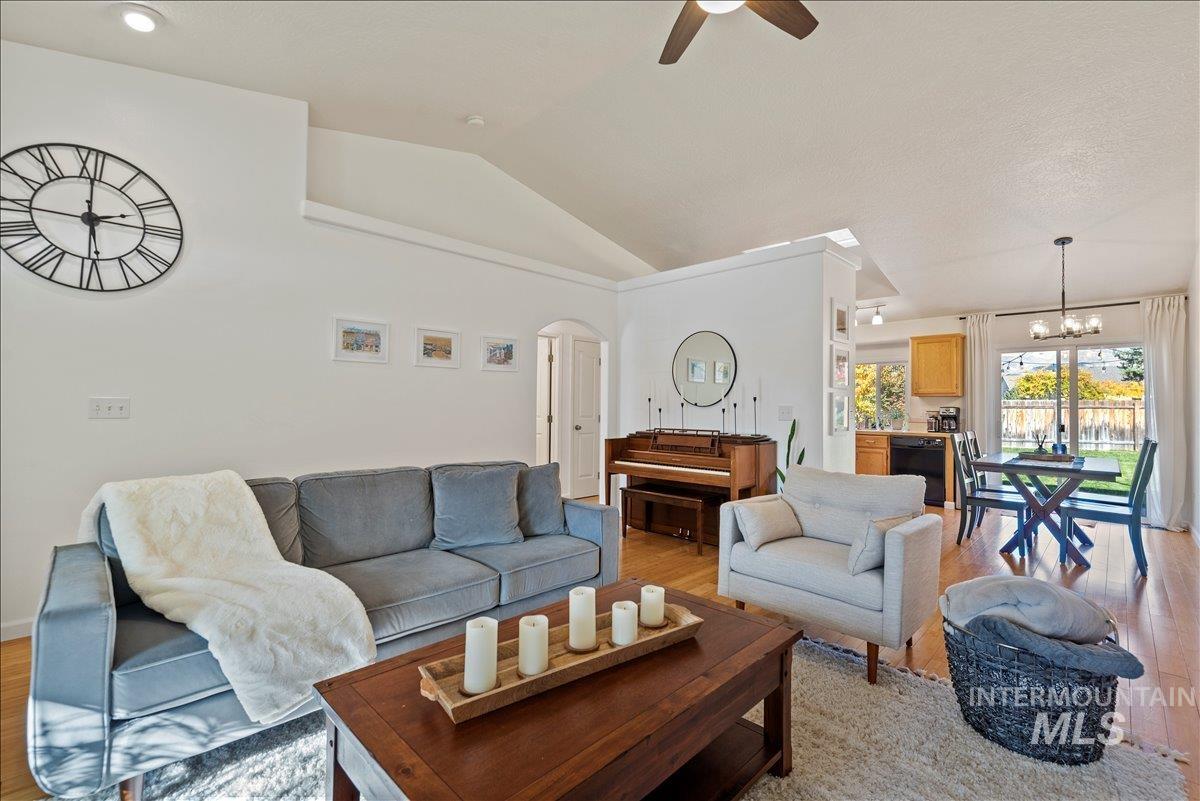 Living room featuring lofted ceiling, light wood-style floors, arched walkways, a ceiling fan, and a chandelier