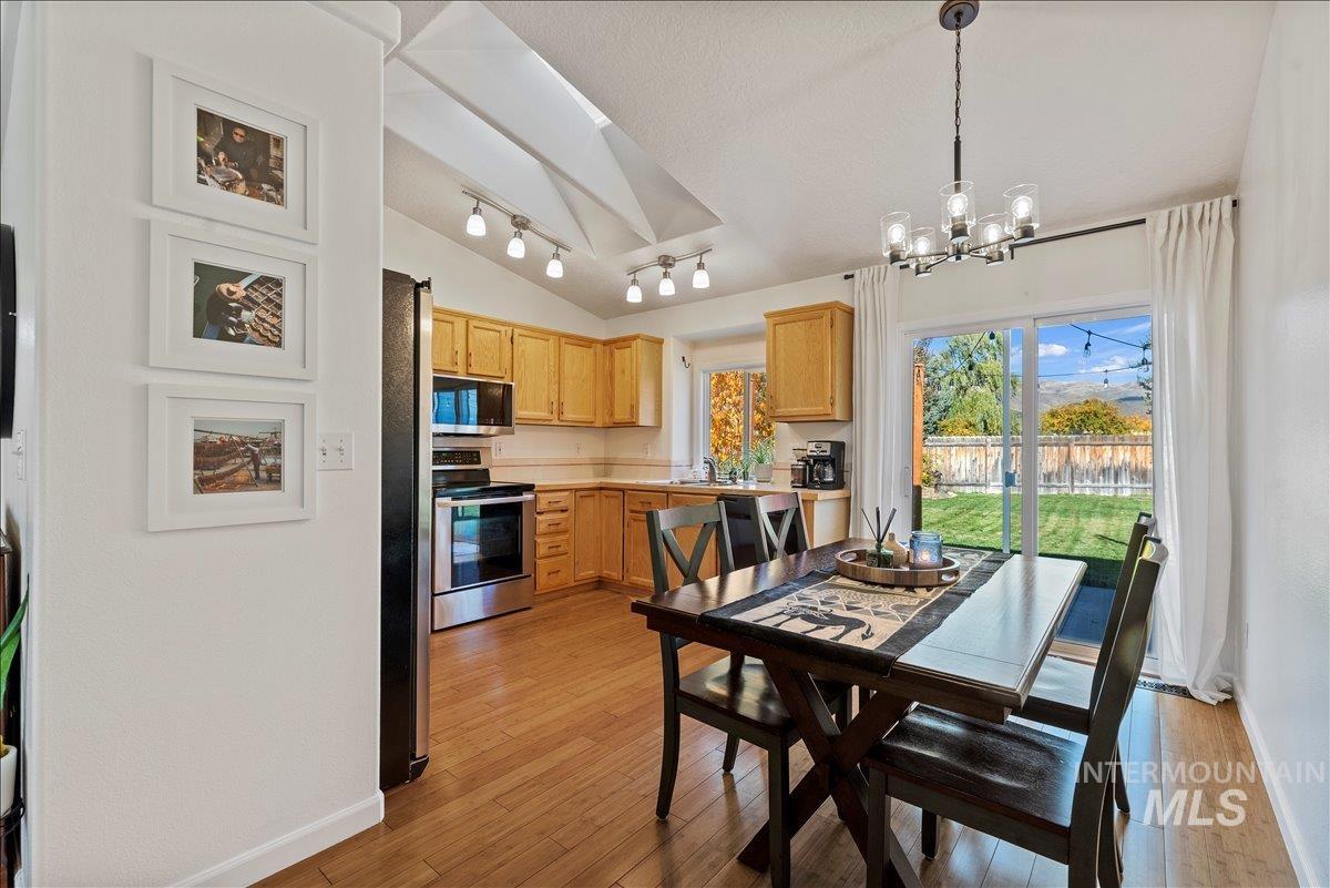Dining space with light wood finished floors, lofted ceiling, track lighting, and a chandelier