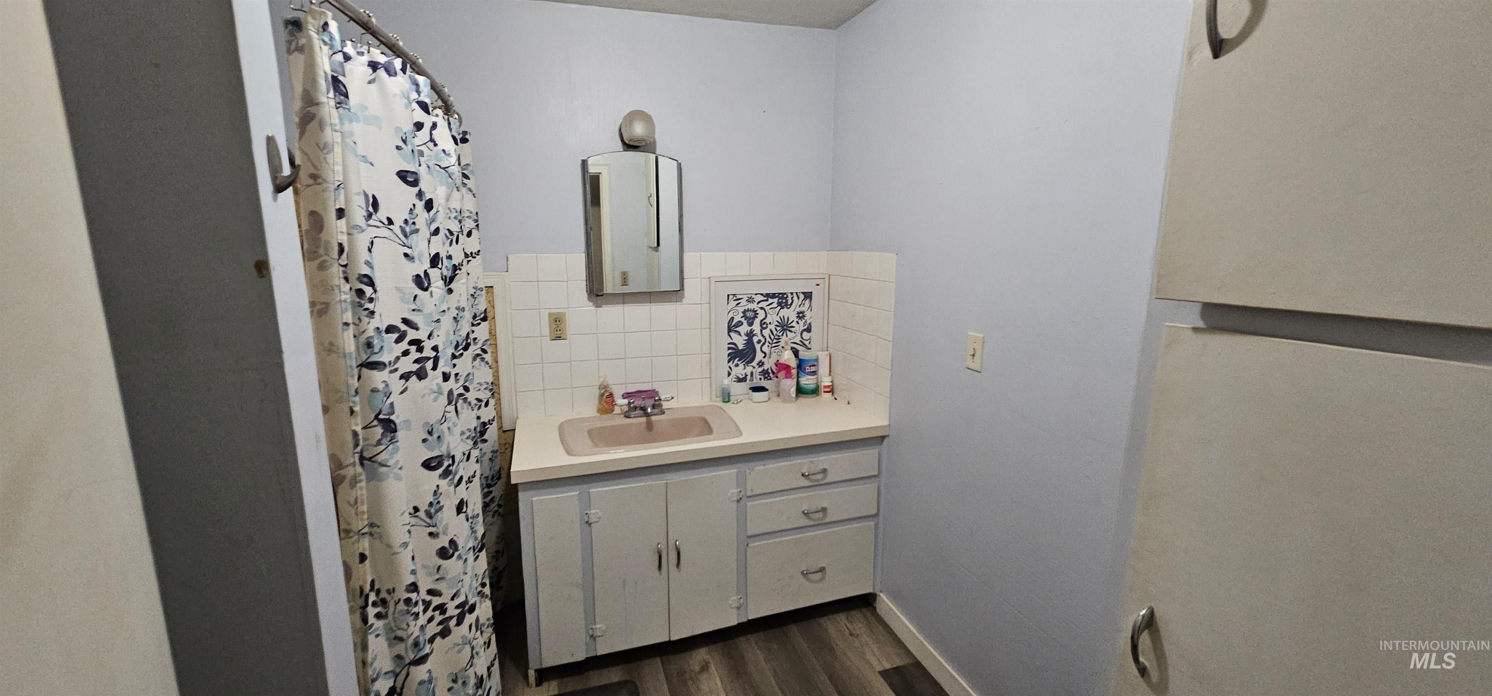 Full bathroom with vanity, a shower with curtain, decorative backsplash, and dark wood-style floors