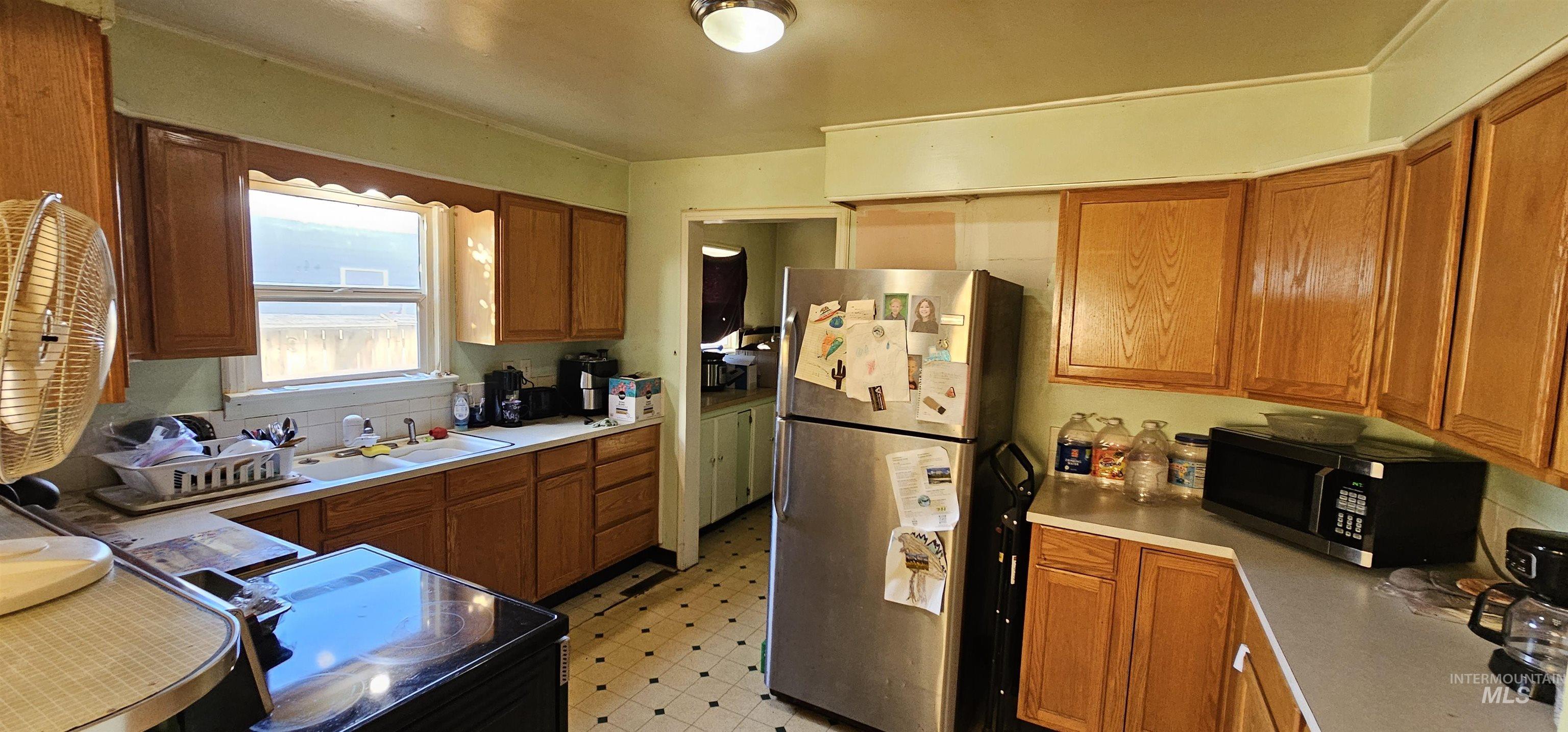 Kitchen featuring brown cabinetry, black appliances, light countertops, and light flooring