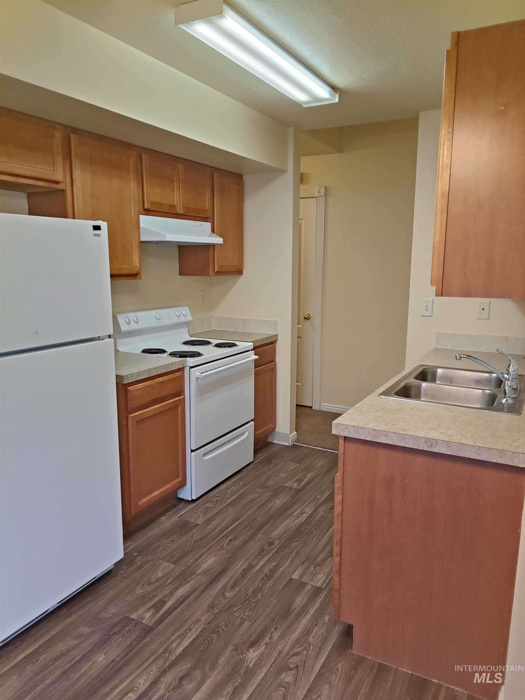 Kitchen with white appliances, dark wood-style flooring, under cabinet range hood, and light countertops
