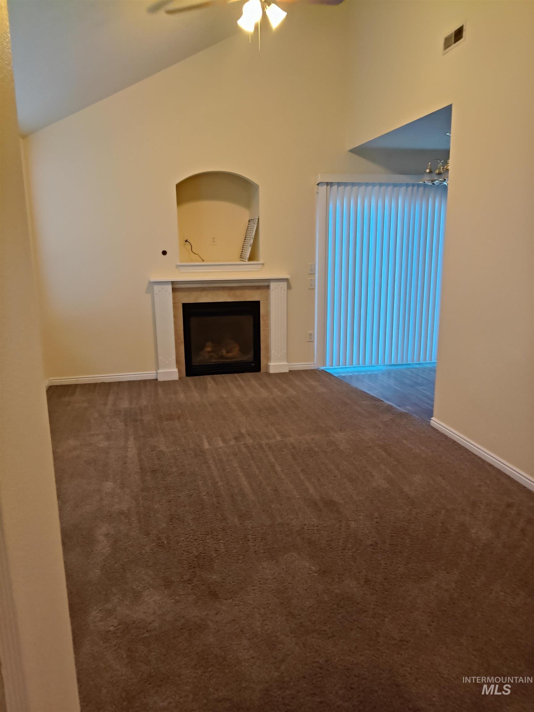 Unfurnished living room featuring a tiled fireplace, dark carpet, ceiling fan, and high vaulted ceiling