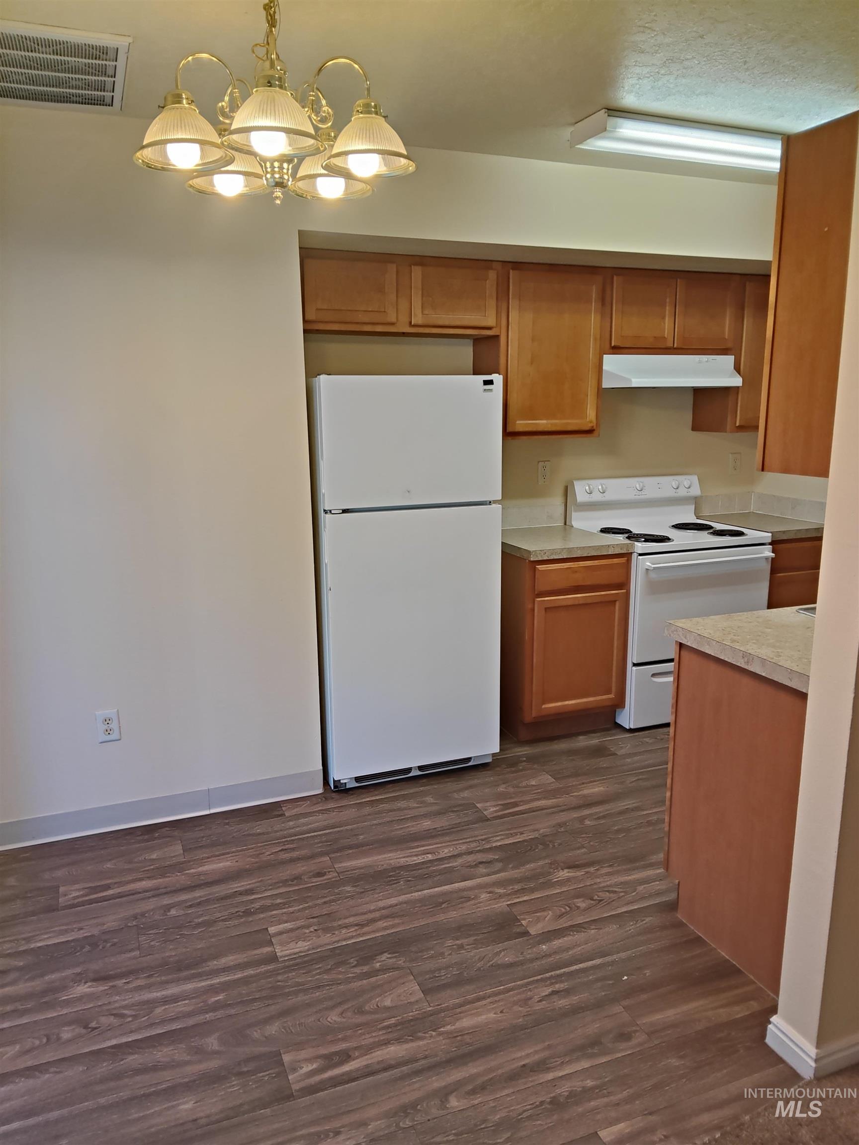 Kitchen with light countertops, white appliances, a chandelier, brown cabinets, and dark wood finished floors