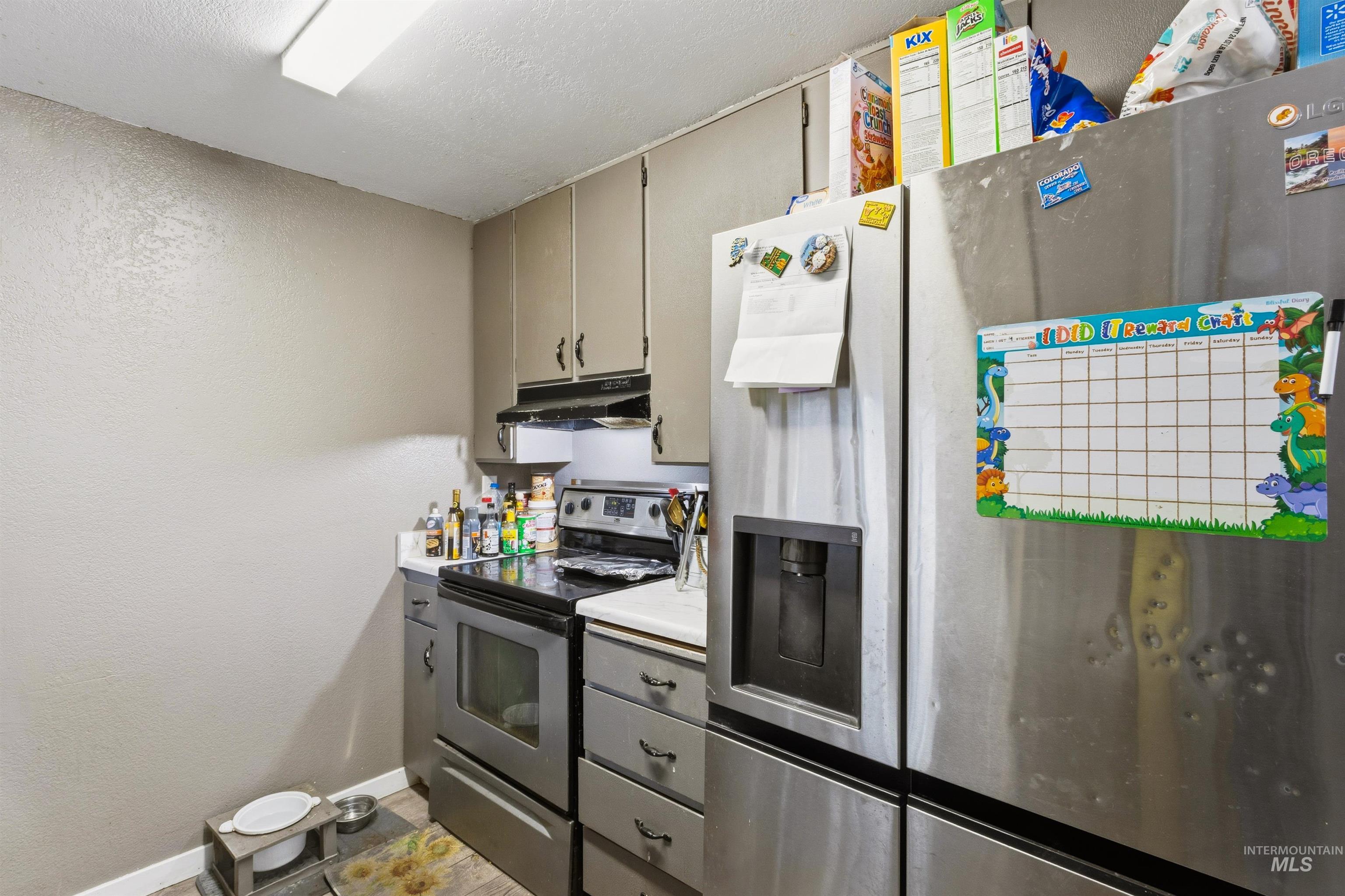 Kitchen with stainless steel appliances, a textured wall, light countertops, under cabinet range hood, and a textured ceiling