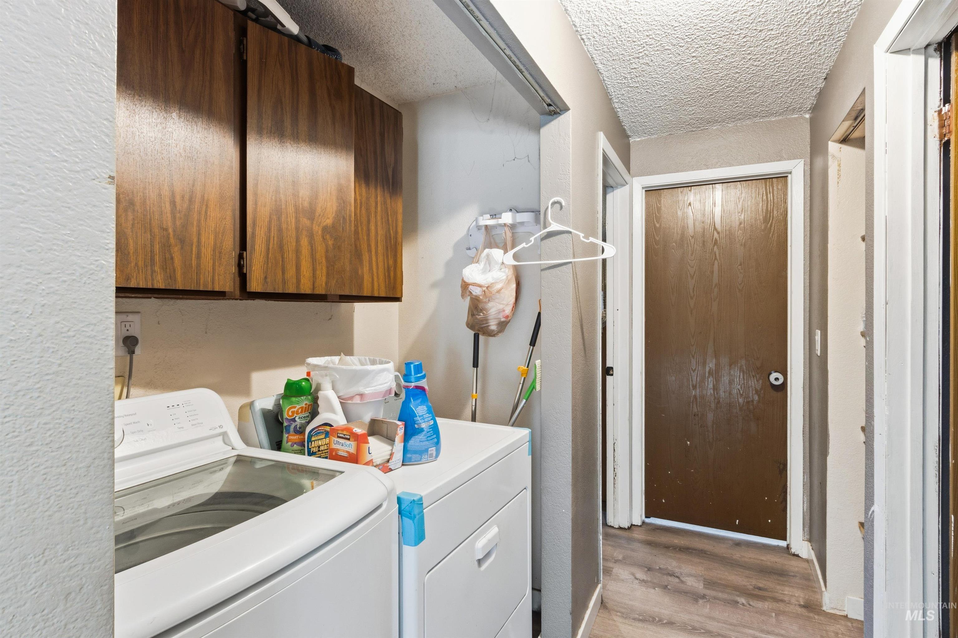 Washroom featuring light wood-style flooring, a textured wall, a textured ceiling, independent washer and dryer, and cabinet space