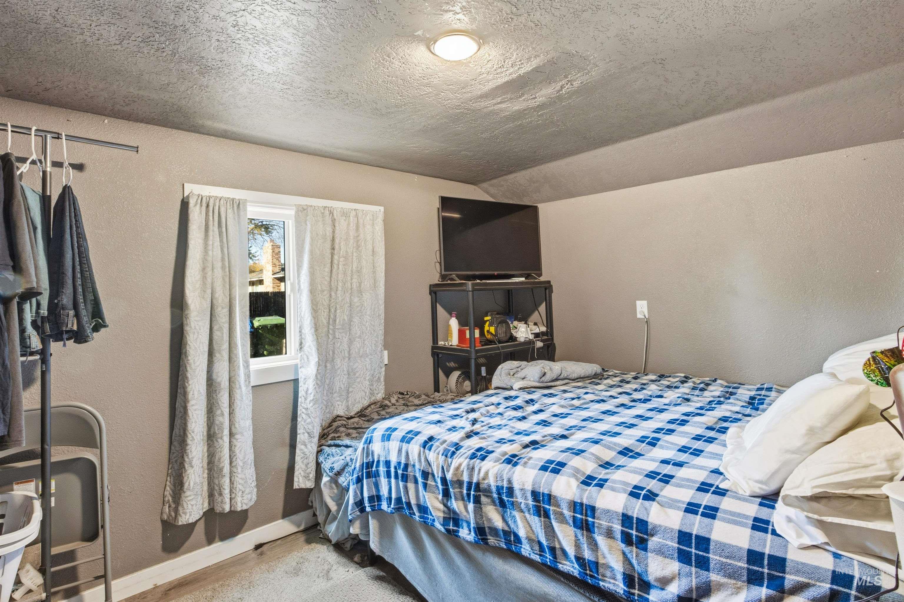Bedroom featuring a textured wall, a textured ceiling, carpet flooring, and lofted ceiling