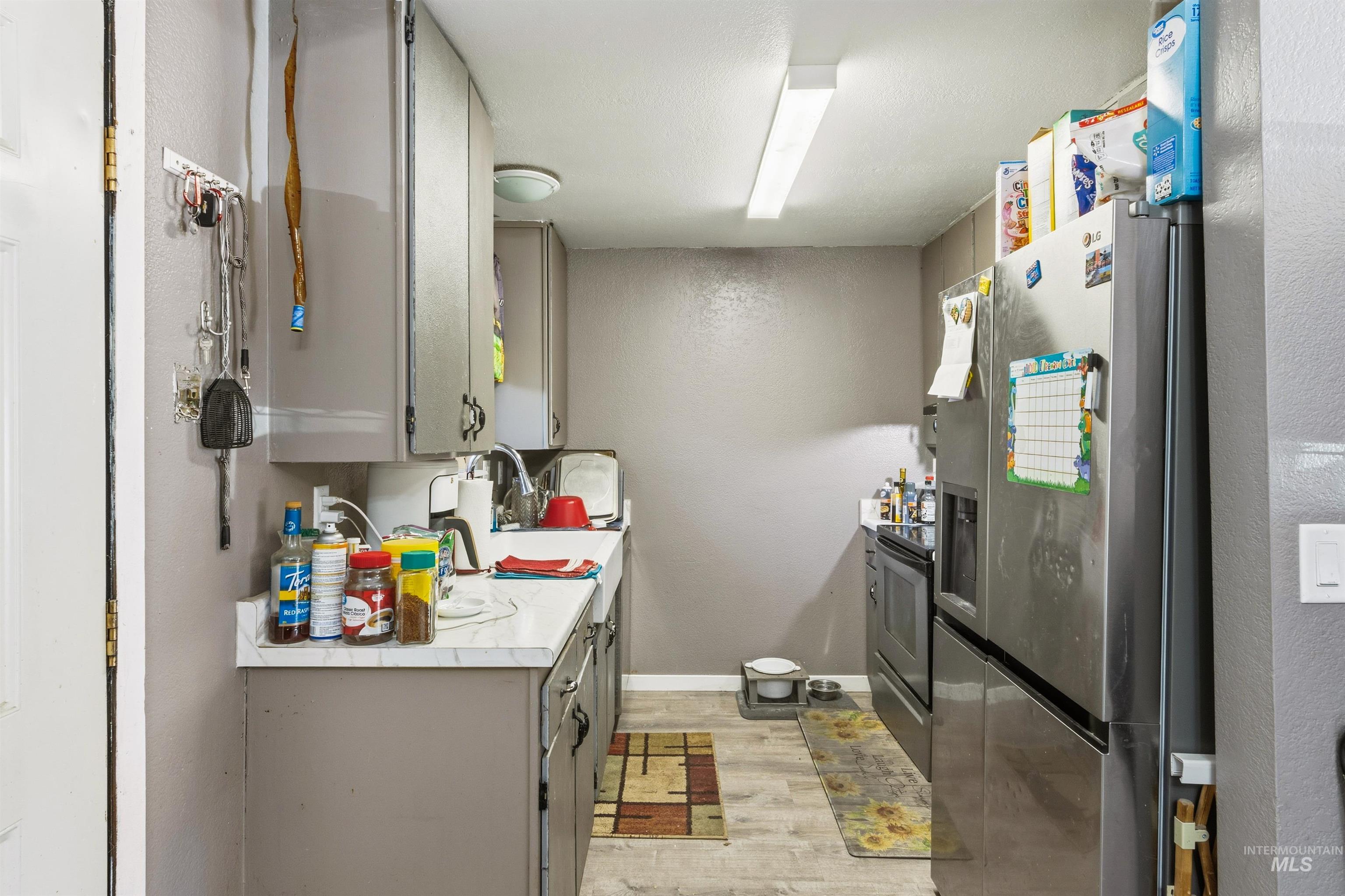 Kitchen featuring light countertops, stainless steel appliances, light wood-style floors, gray cabinetry, and a textured wall