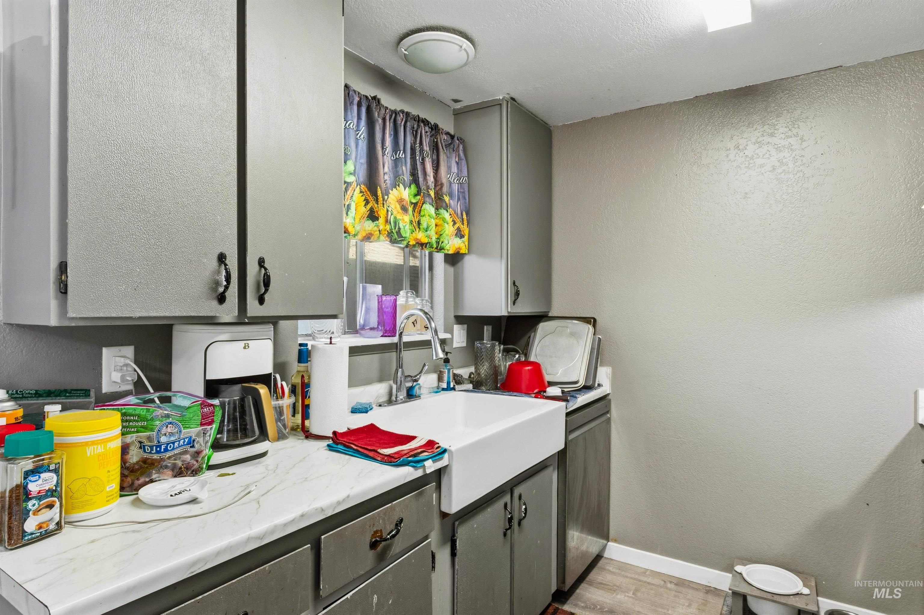Kitchen featuring a textured wall, gray cabinetry, light countertops, light wood finished floors, and a textured ceiling