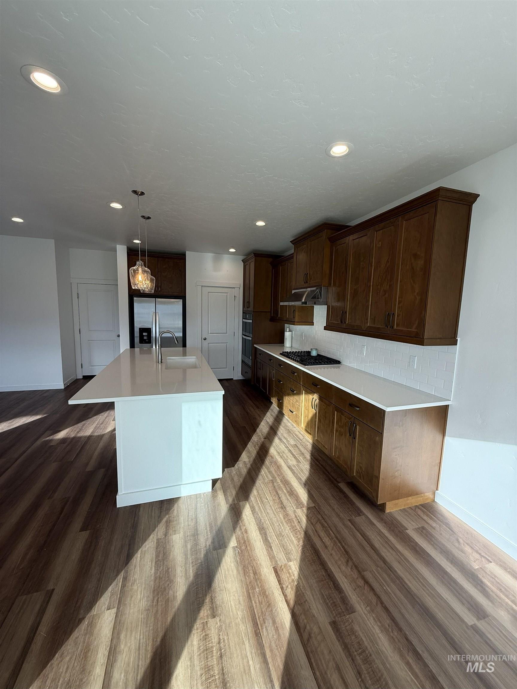 Kitchen with an island with sink, dark wood-style floors, stainless steel appliances, dark brown cabinetry, and recessed lighting