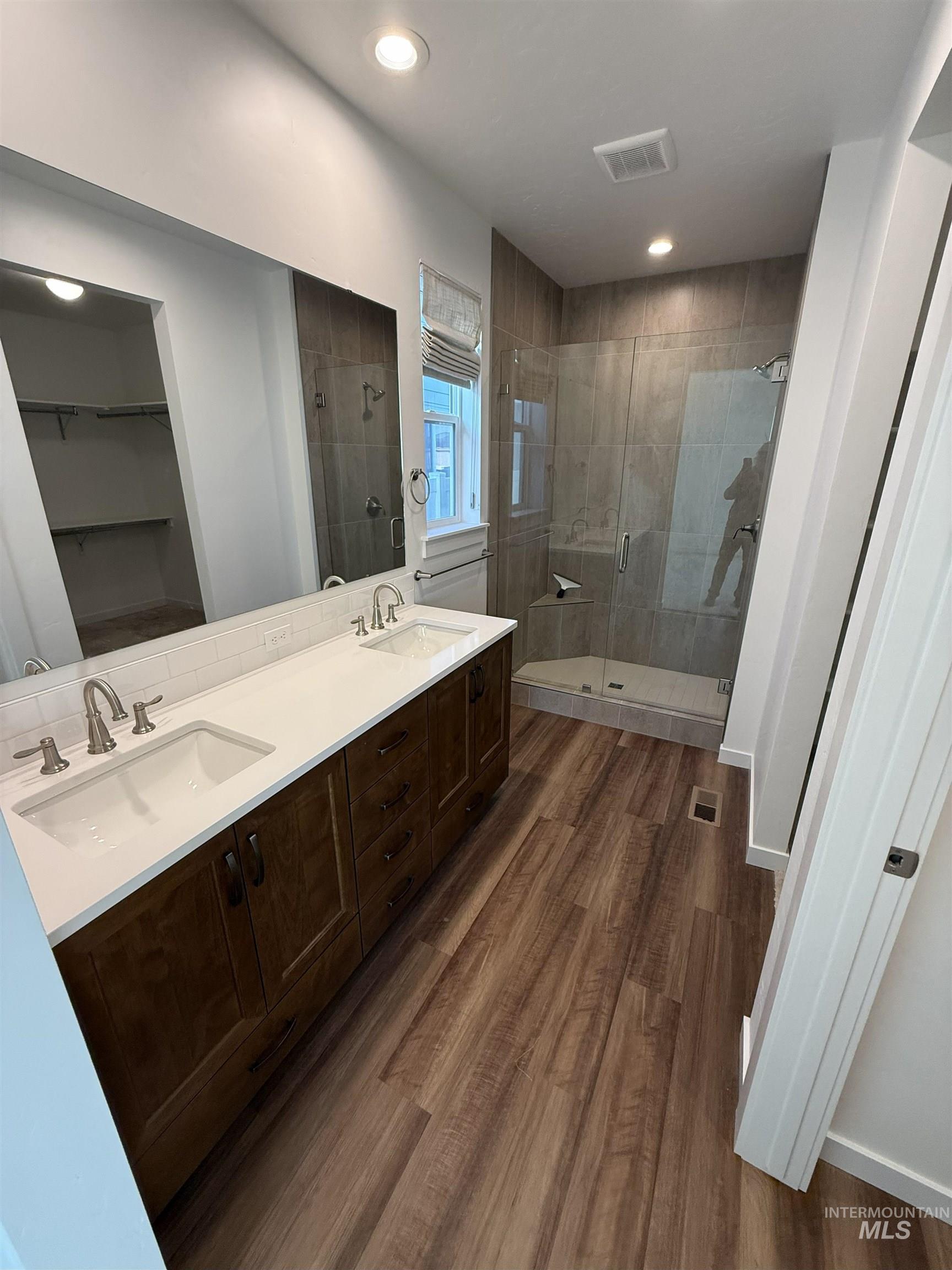 Primary bathroom featuring a spacious closet, double vanity, a stall shower, dark wood-style flooring, and recessed lighting